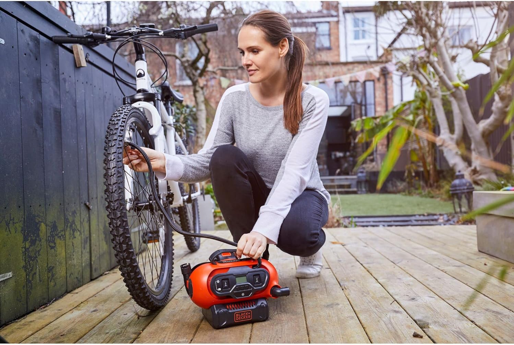 Kobieta pompuje oponę roweru pomarańczowym urządzeniem na drewnianym tarasie.