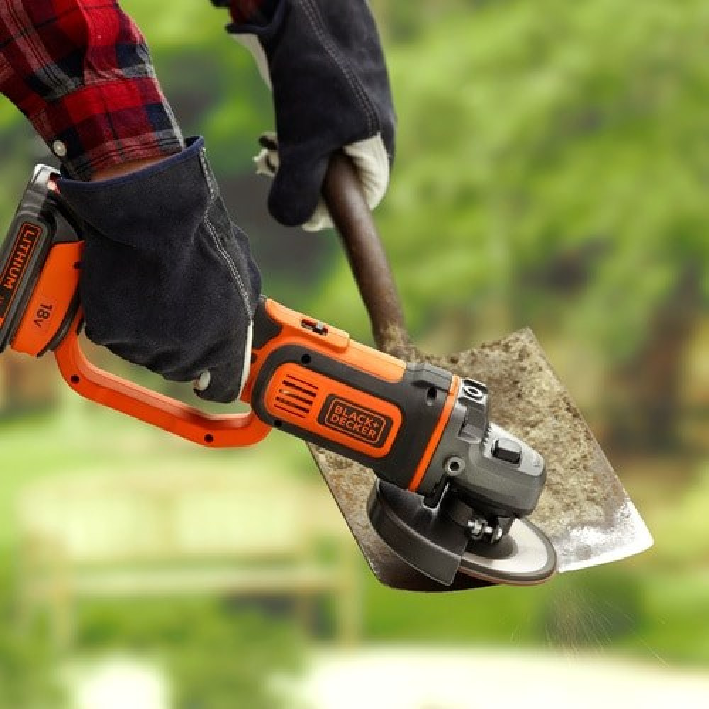 Osoba w rękawiczkach ostrzy łopatę szlifierką kątową na zewnątrz.