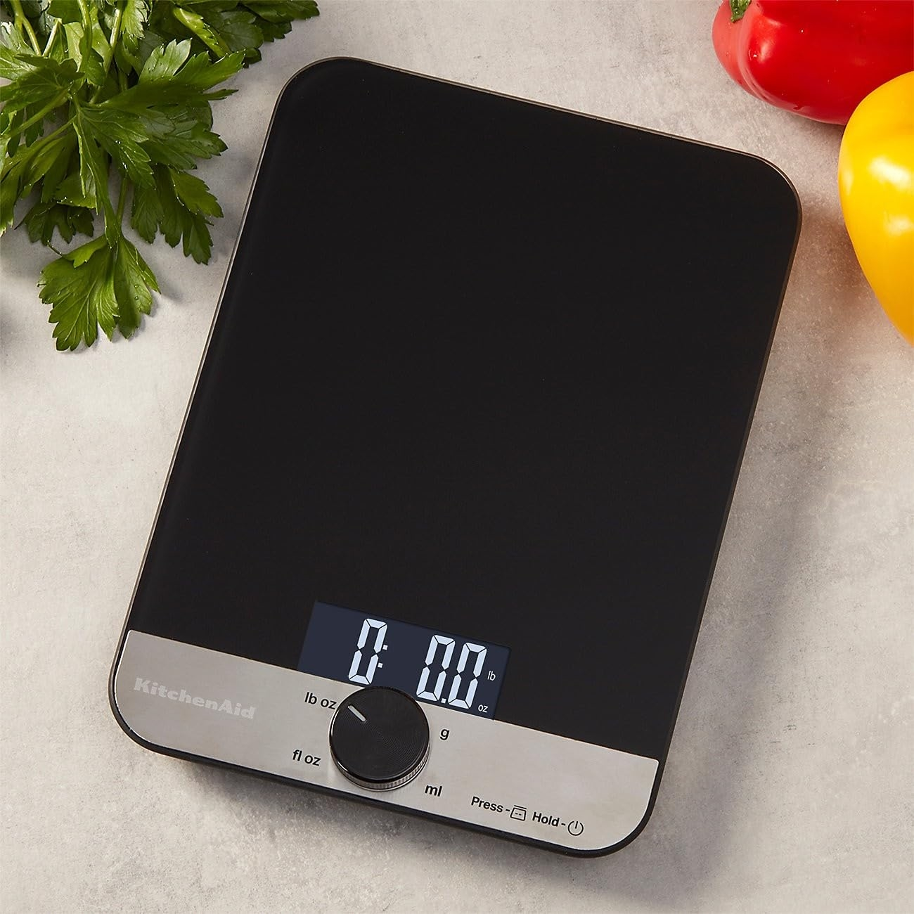 Schwarze Küchenwaage mit digitaler Anzeige, daneben Petersilie und Paprika.