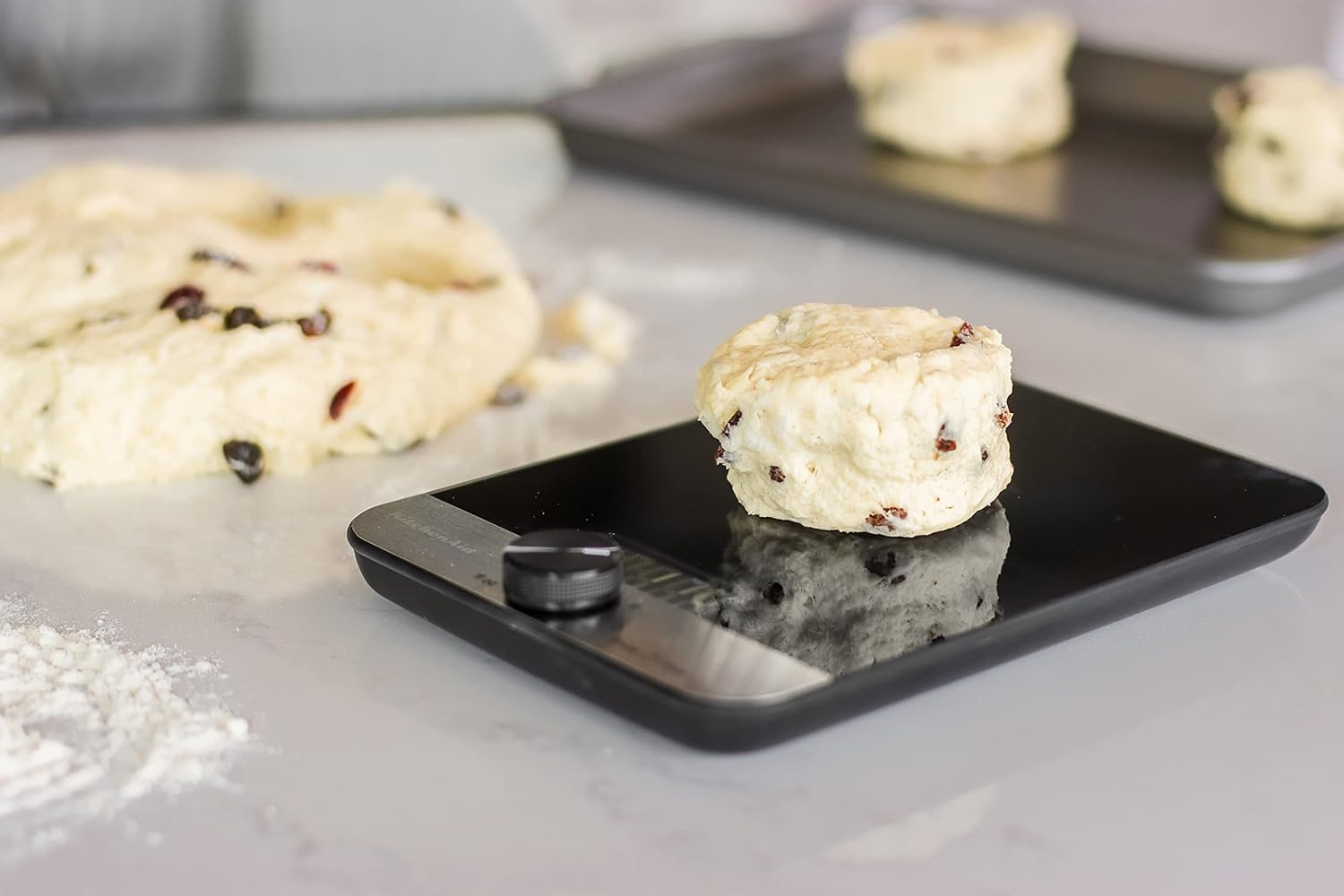 Ein einzelner Scone mit Rosinen liegt auf einer schwarzen Küchenwaage.