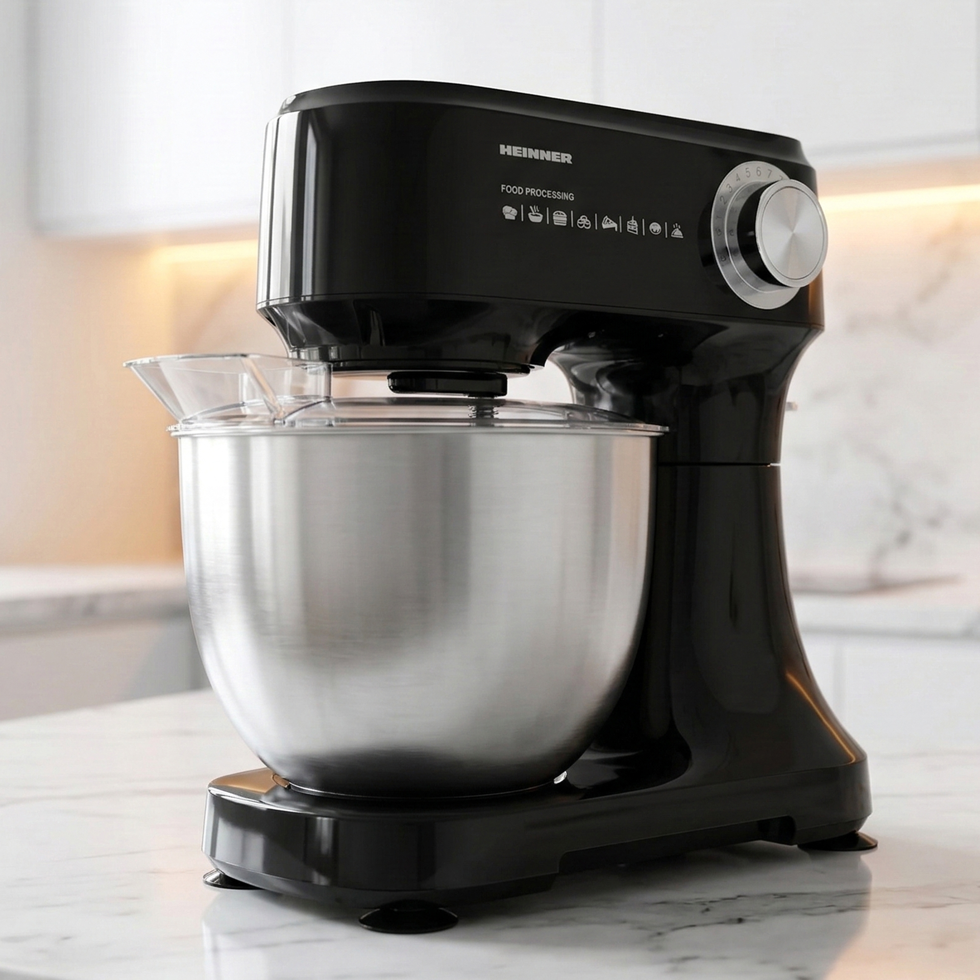 Black kitchen mixer with stainless steel bowl and clear splash guard on marble countertop.