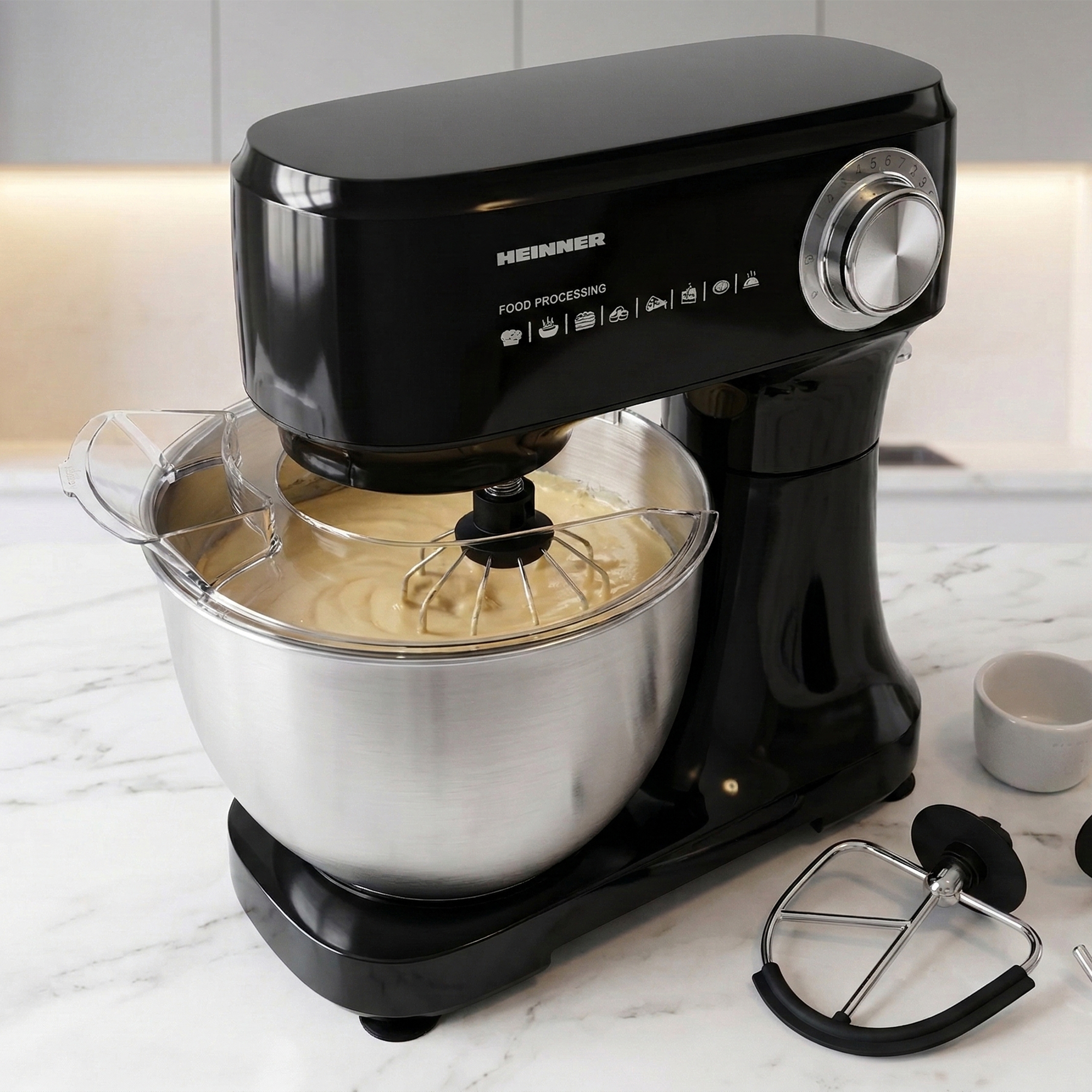 Black kitchen mixer with stainless steel bowl and batter, on marble countertop.