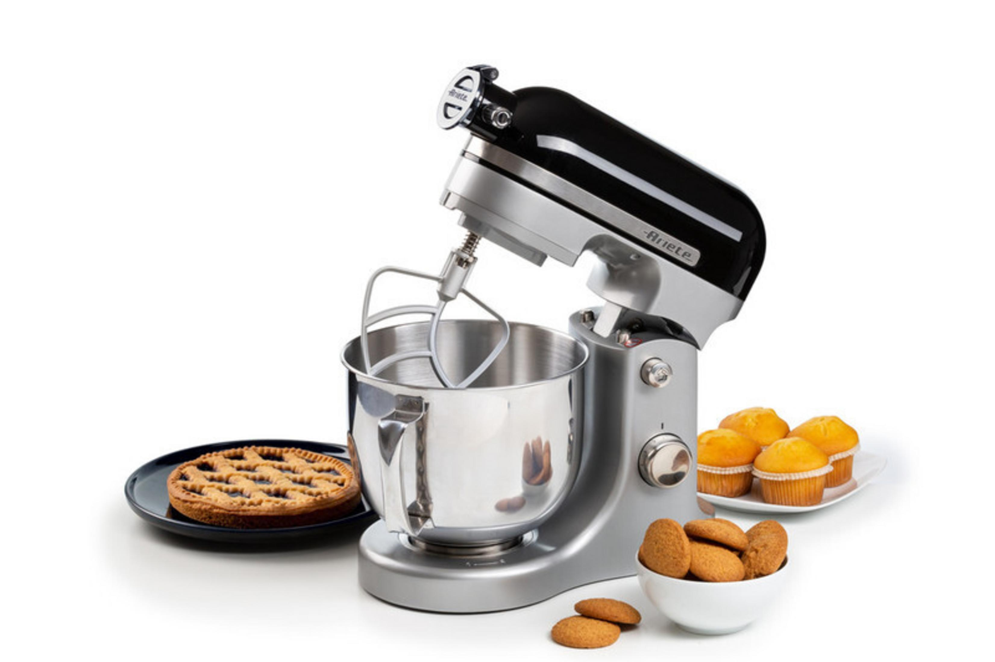 Ein silberner Küchenmixer mit schwarzer Oberseite, daneben ein Kuchen und Muffins.