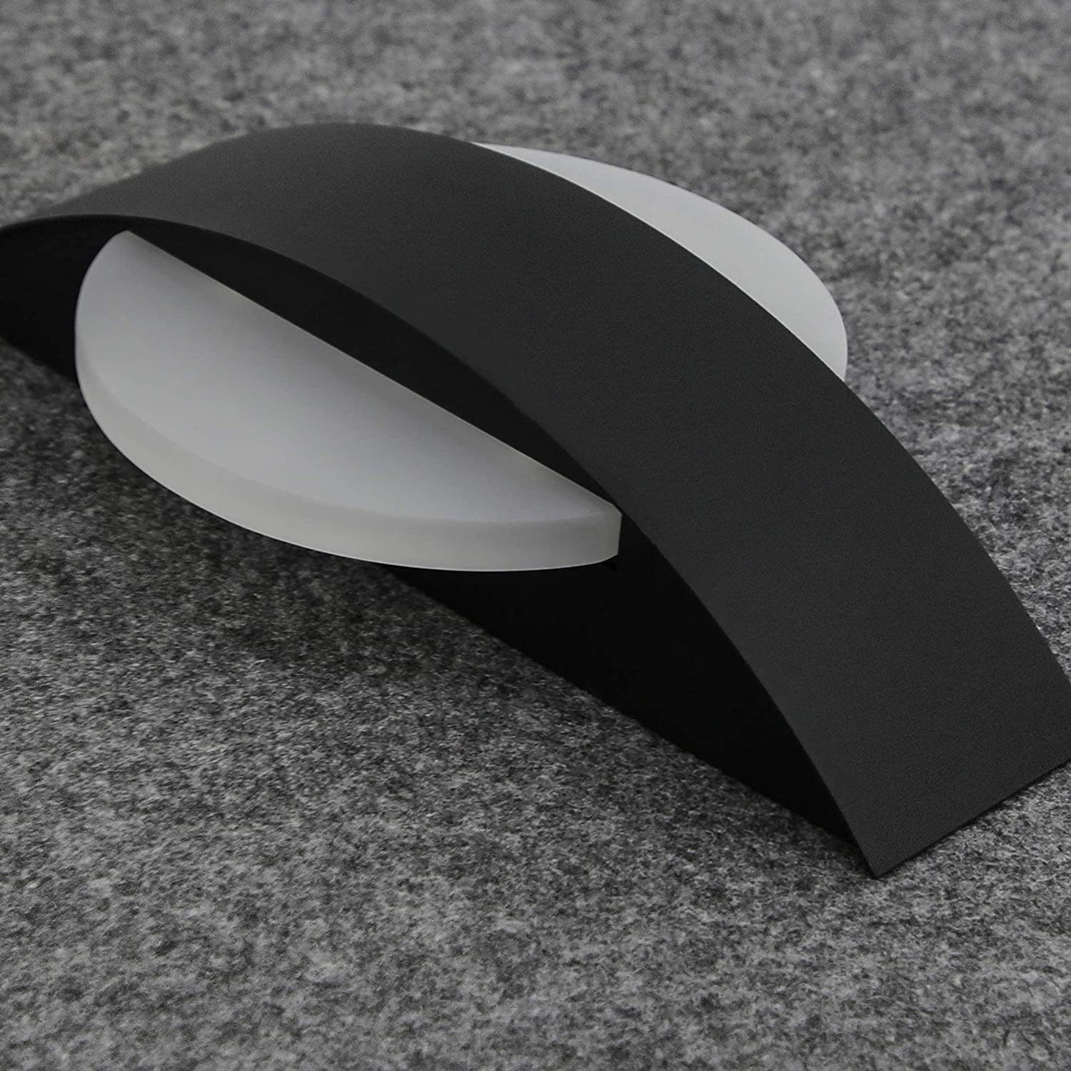 Un nastro nero curva su un disco bianco opaco su tessuto grigio.