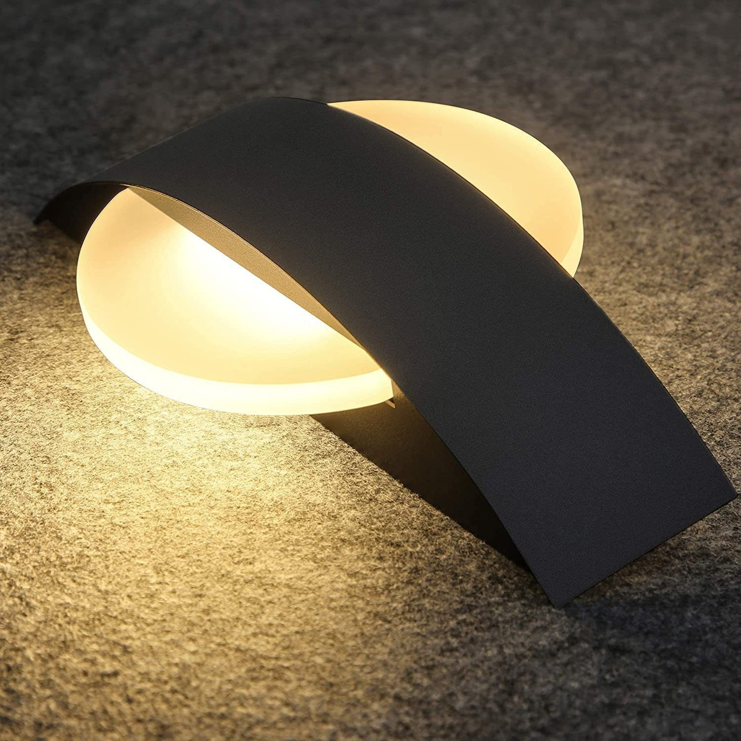 Una lampada da parete moderna grigio scuro dal design curvo, che emette una luce calda e soffusa.