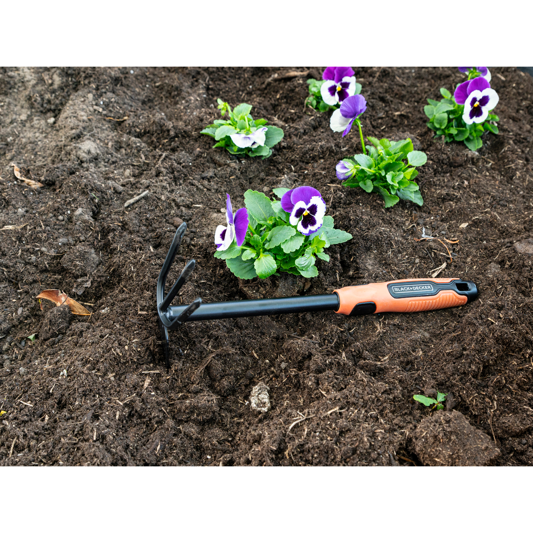 Tuinwerktuig met oranje handvat ligt naast paarse en witte viooltjes in de aarde.
