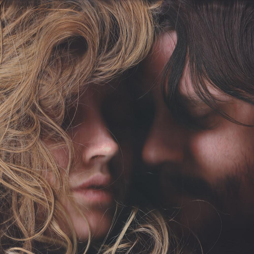 Close-up van twee gezichten die elkaar raken, blonde vrouw links, donker haar rechts.