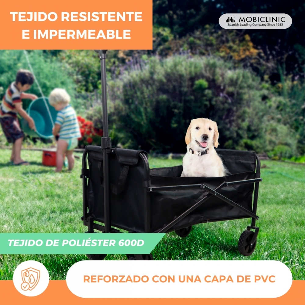 Un labrador se sienta en un carro negro en un jardín. Niños juegan al fondo.