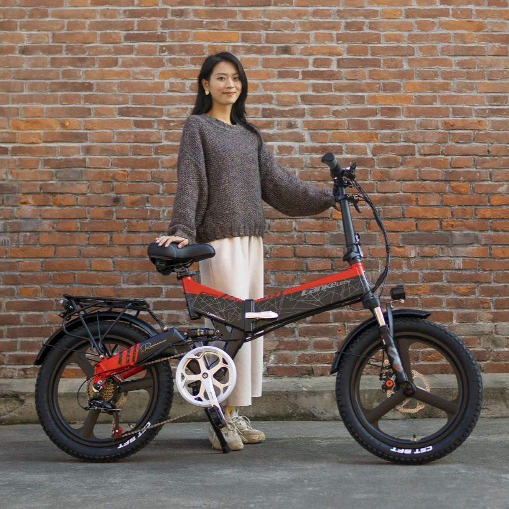 Una mujer está junto a una bicicleta plegable roja y negra contra una pared de ladrillos.