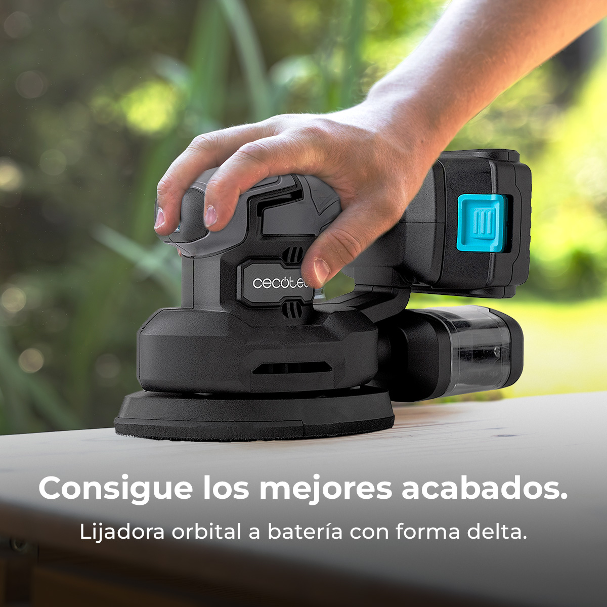 Una mano tiene una levigatrice nera con pulsante blu, all'aperto.