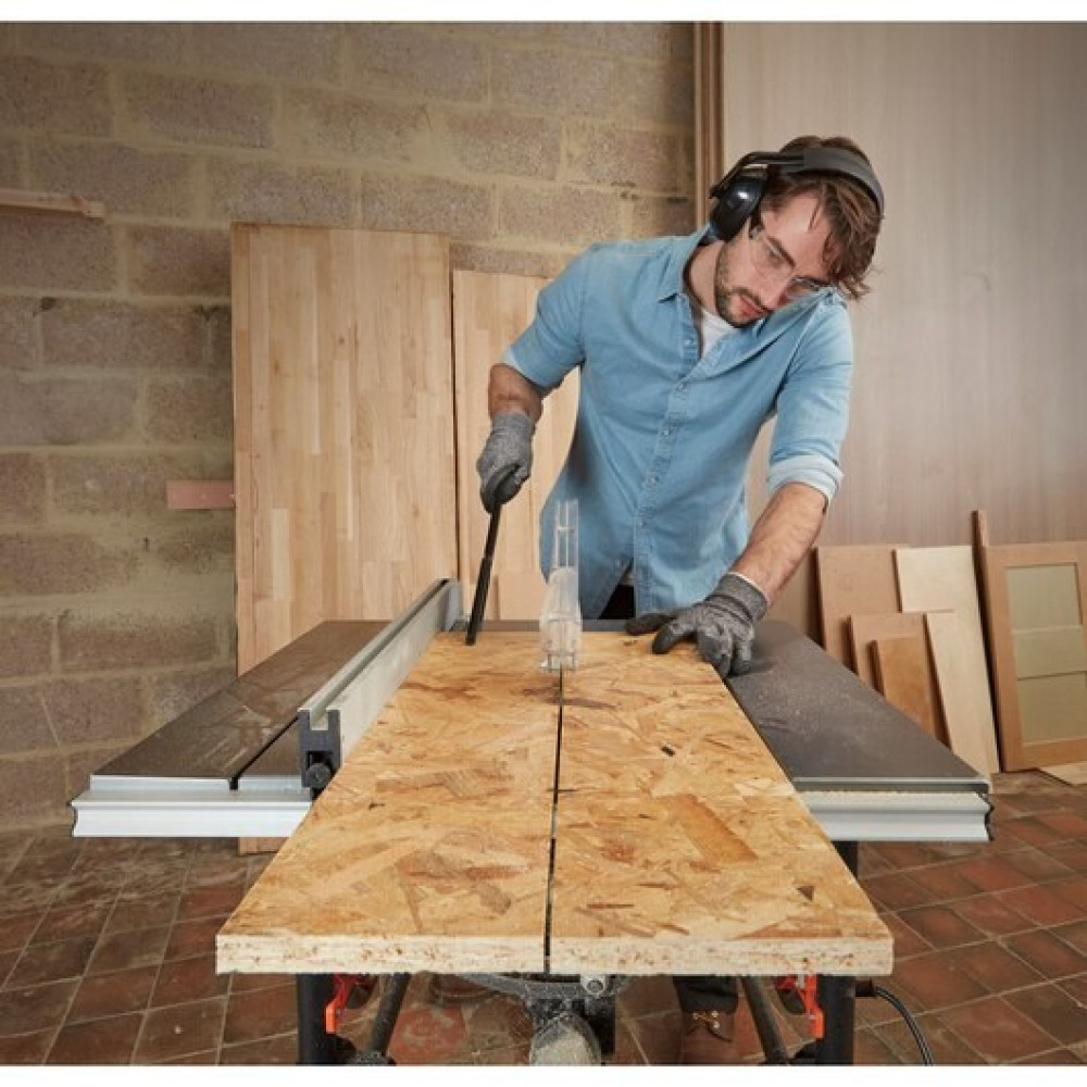 Mężczyzna w okularach ochronnych i słuchawkach tnie drewno na pile stołowej.