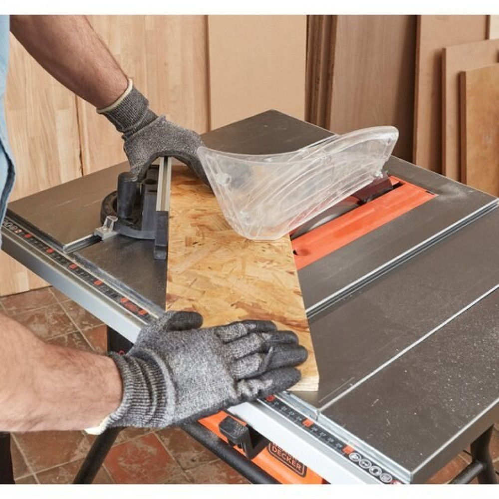 Mężczyzna w rękawiczkach tnie drewno na pile stołowej. Metalowy stół, osłona.