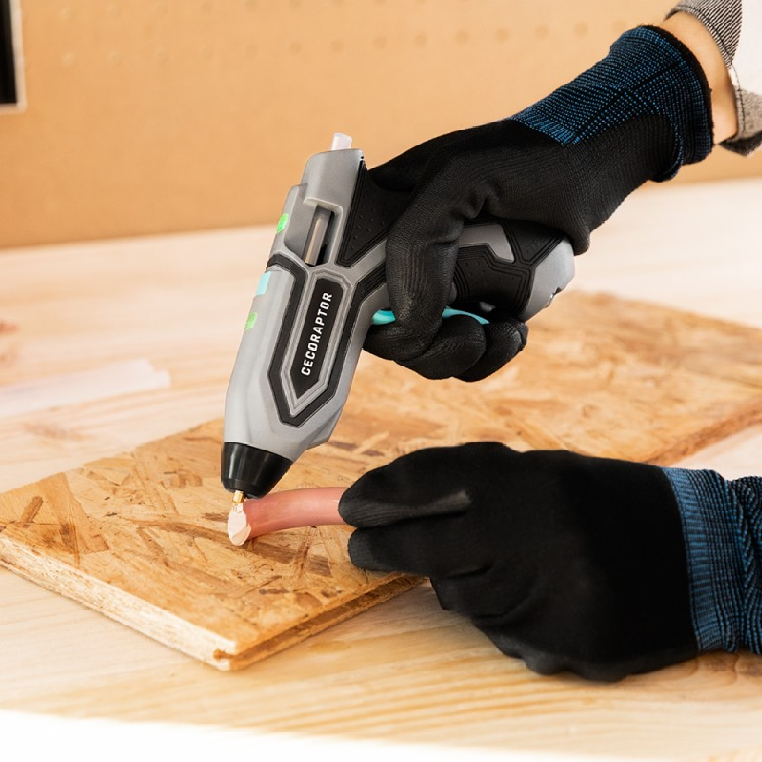 Una mano enguantada usa una pistola de pegamento en madera.