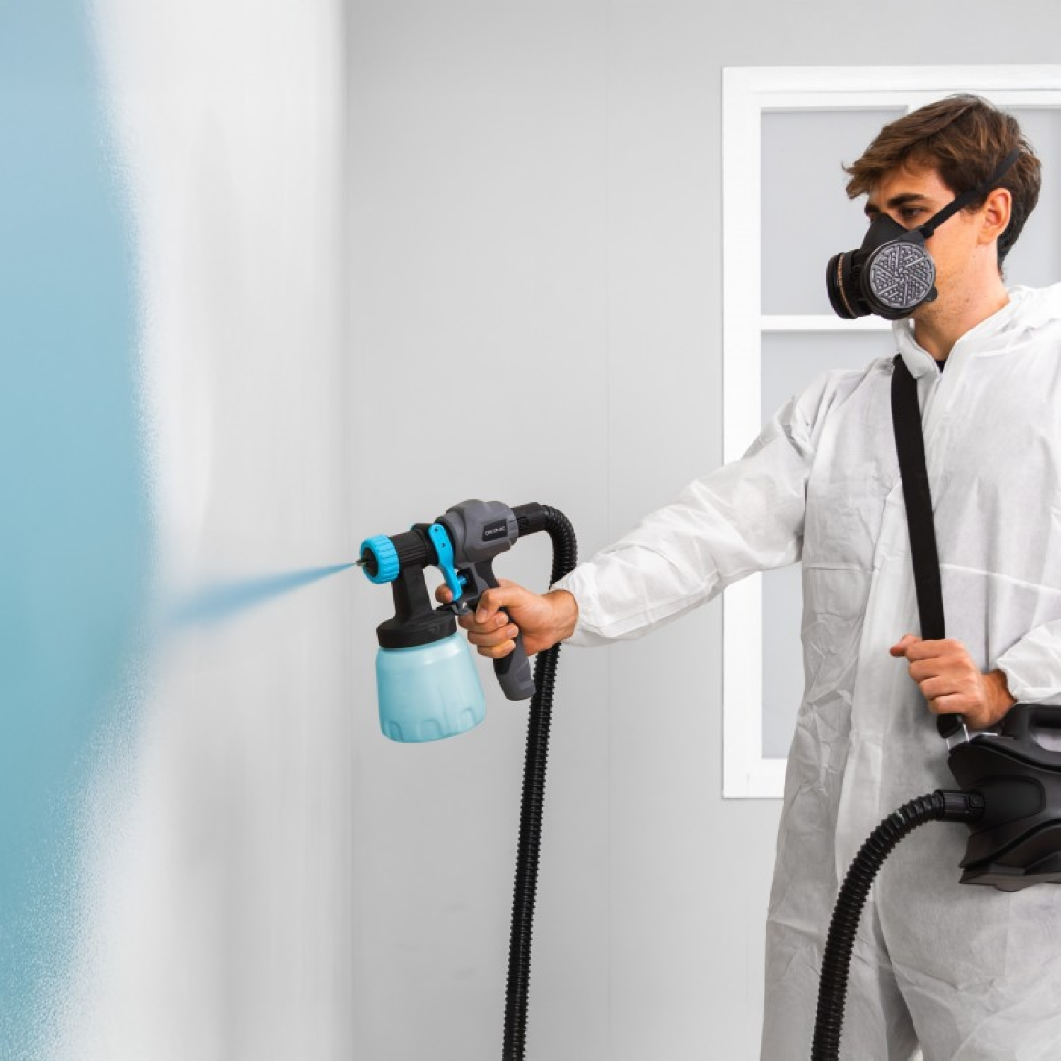 Hombre con traje protector rocía pintura azul en una pared con pistola.