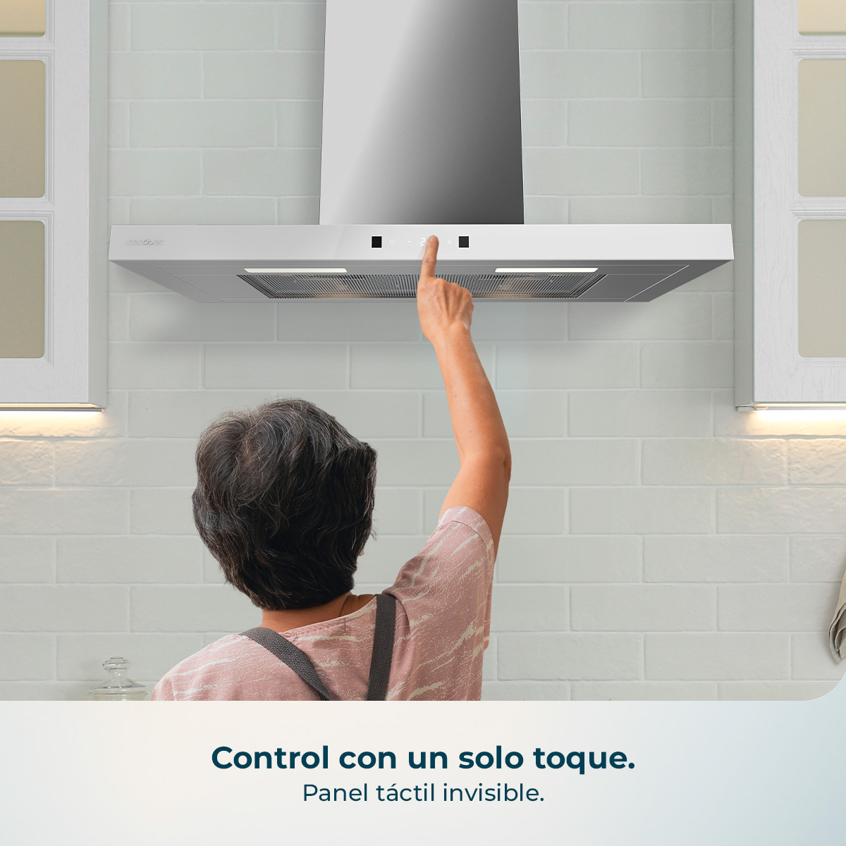 Una mujer opera una campana extractora con controles táctiles en una pared de azulejos blancos.