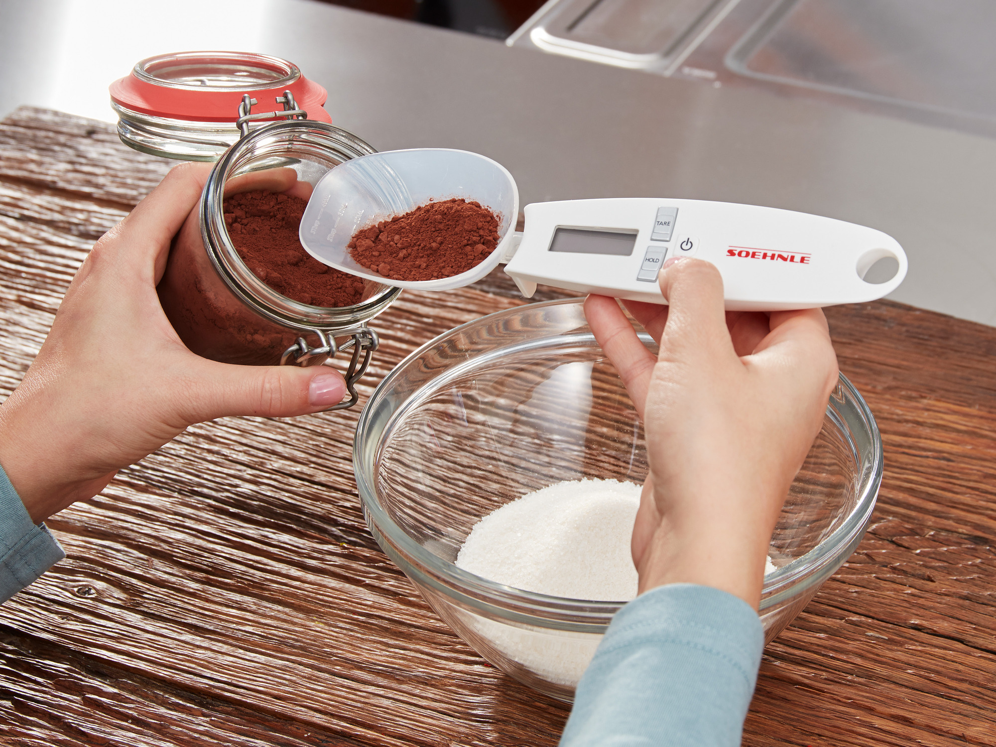 Hände schaufeln Kakaopulver aus Glas mit digitaler Waage in Zuckerschüssel.