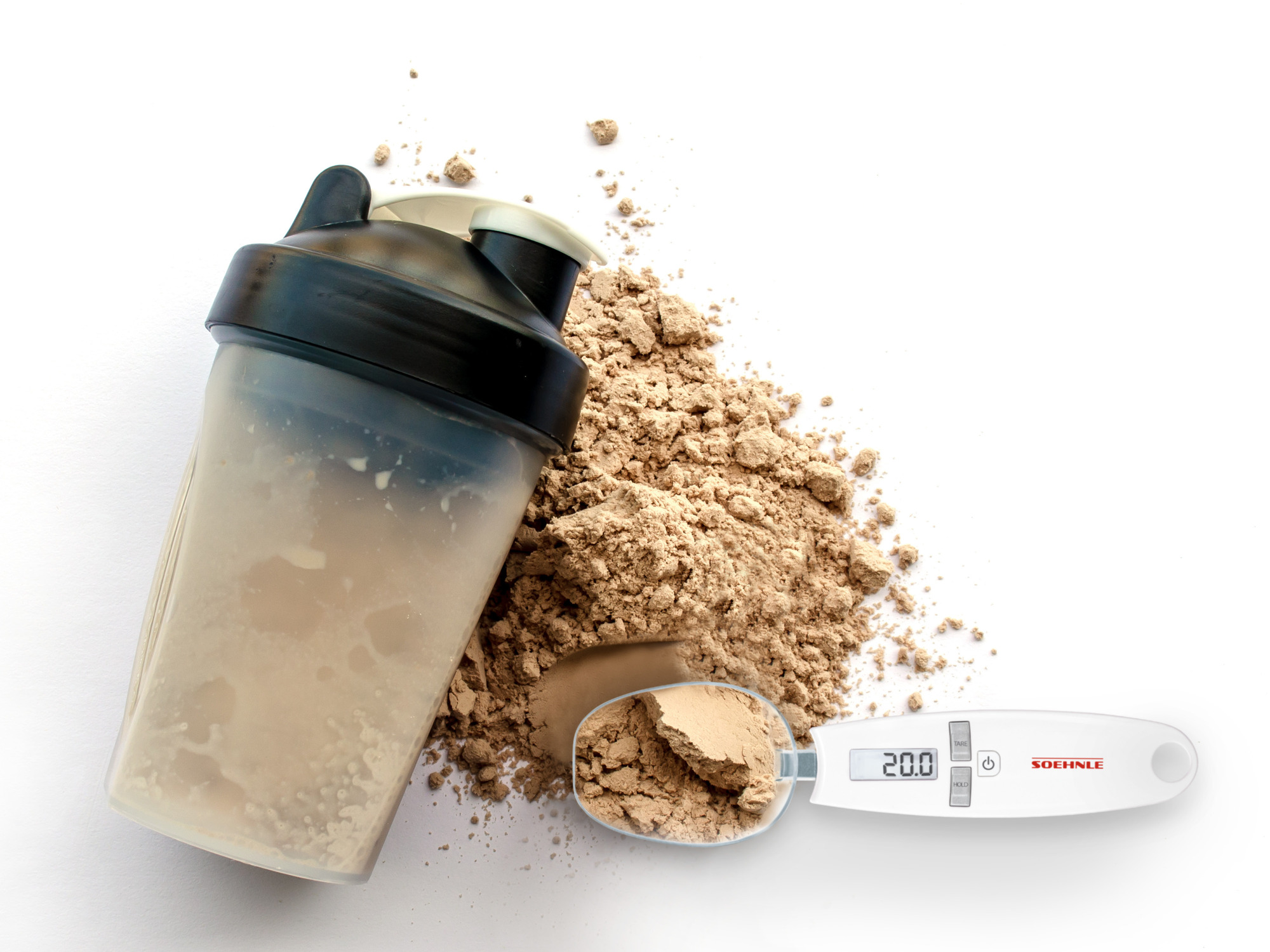 Ein Shaker mit Protein, Löffel und Waage auf weißem Hintergrund.