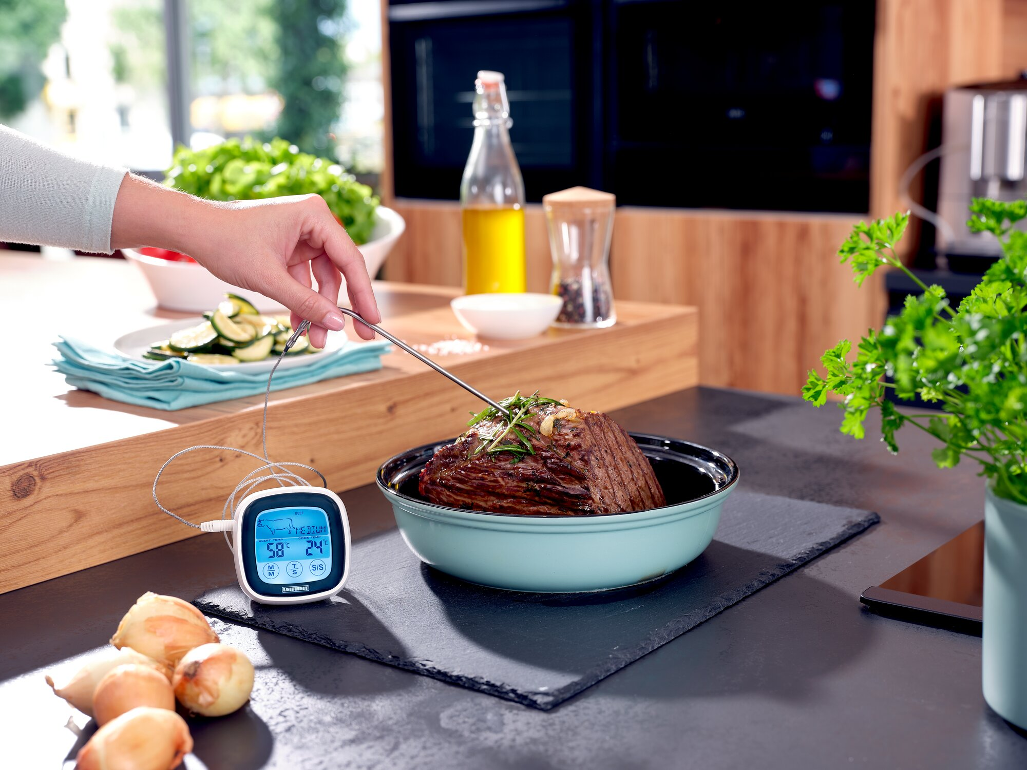 Fleischthermometer prüft Braten in Schüssel, daneben Zwiebeln und digitale Anzeige.
