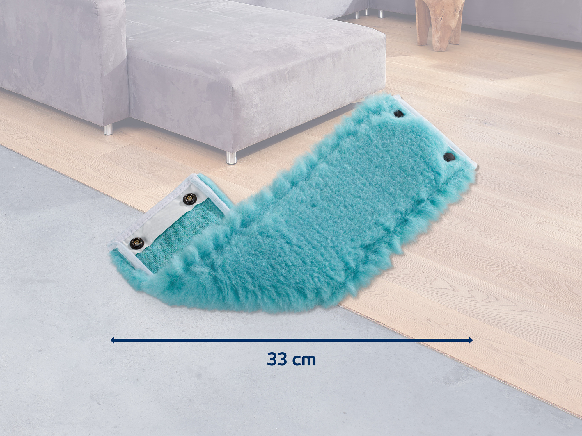 Ein türkiser Wischmoppkopf mit Fell auf einem Holzboden neben einem Sofa.