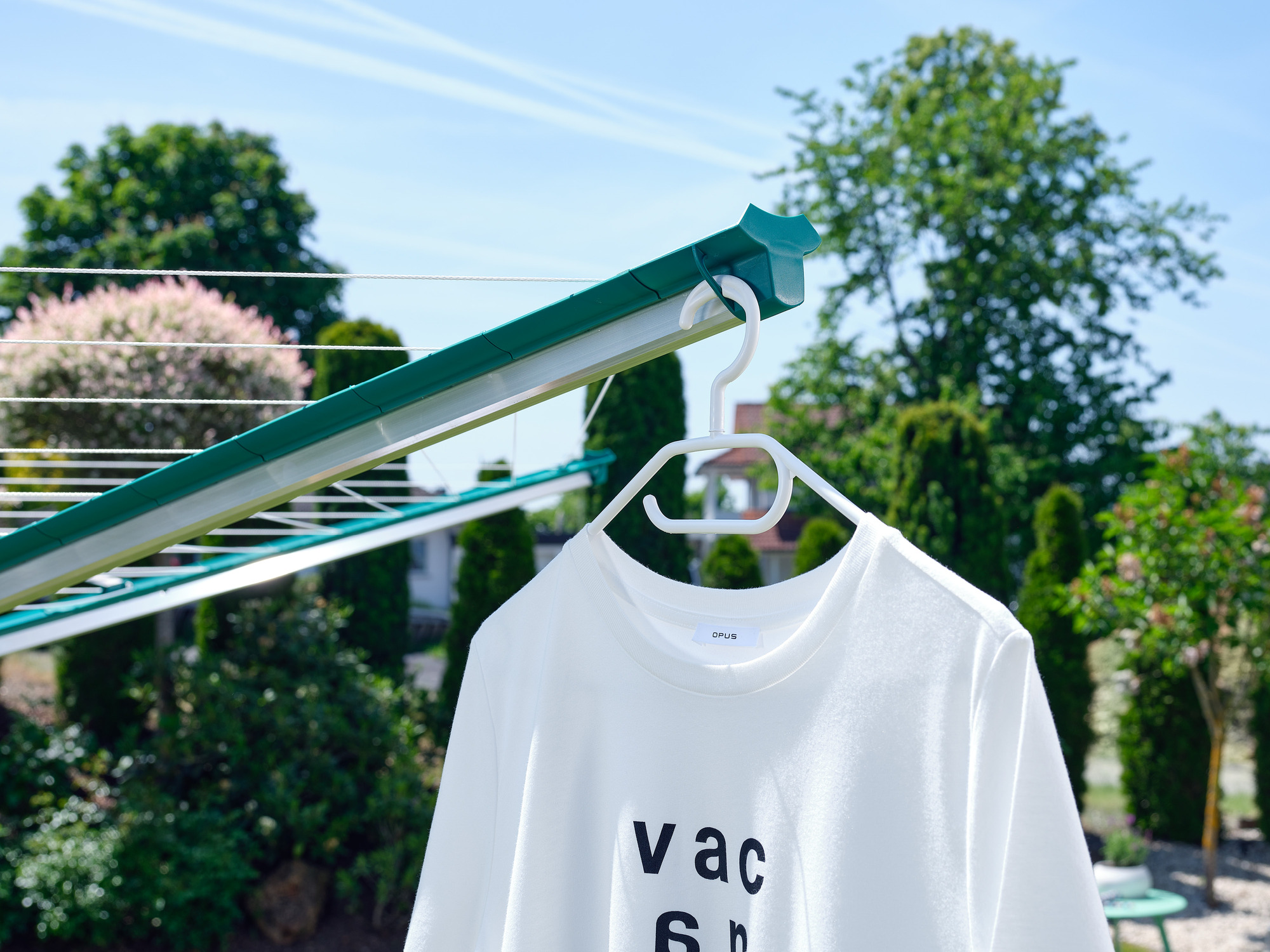Ein weißes T-Shirt mit schwarzer Schrift hängt auf einem Kleiderbügel auf einem Wäscheständer im Freien.