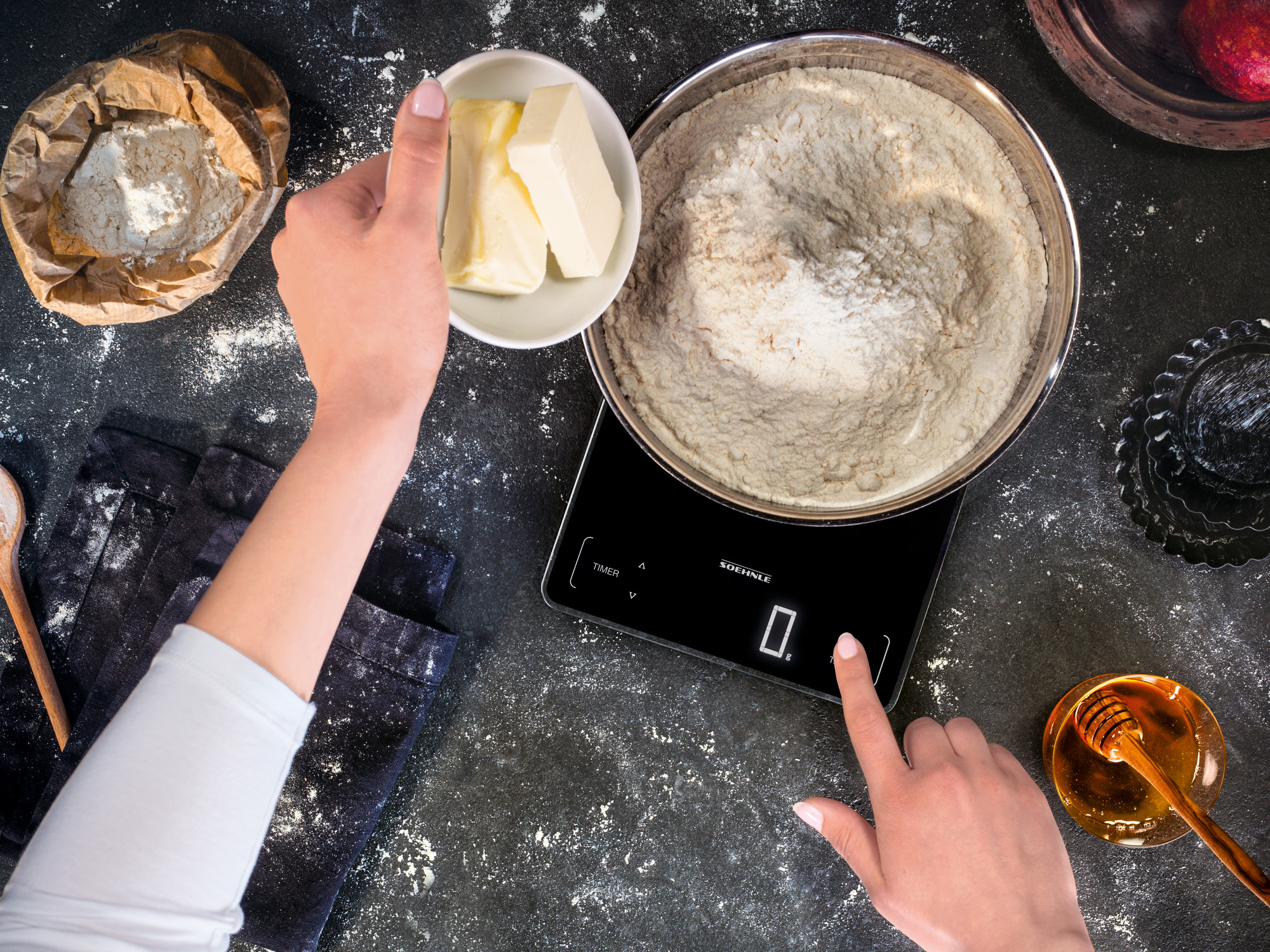 Dłonie ważące mąkę i masło do składników wypieków na czarnej powierzchni.