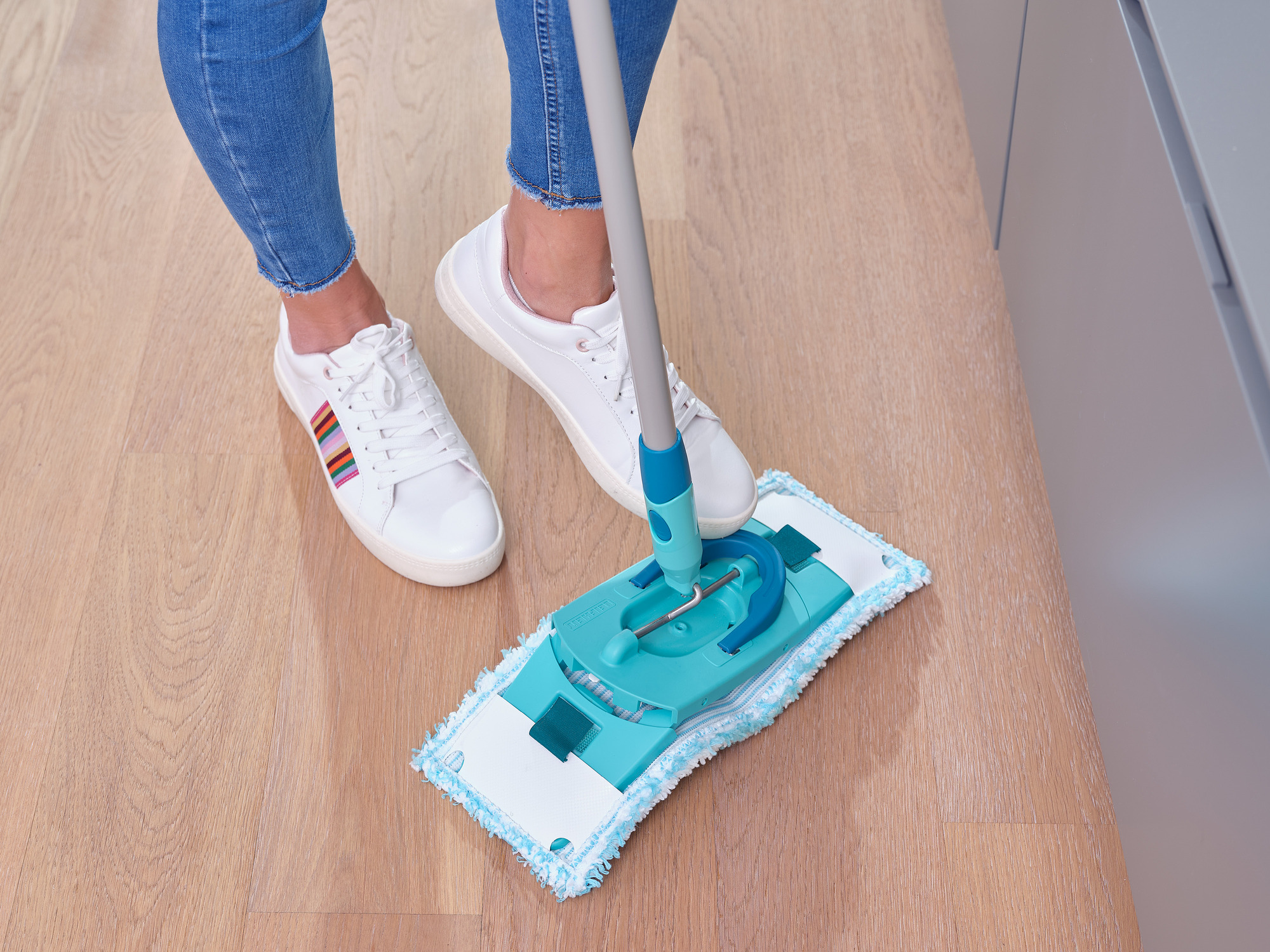Person in Jeans wischt den Holzboden mit einem Mopp.