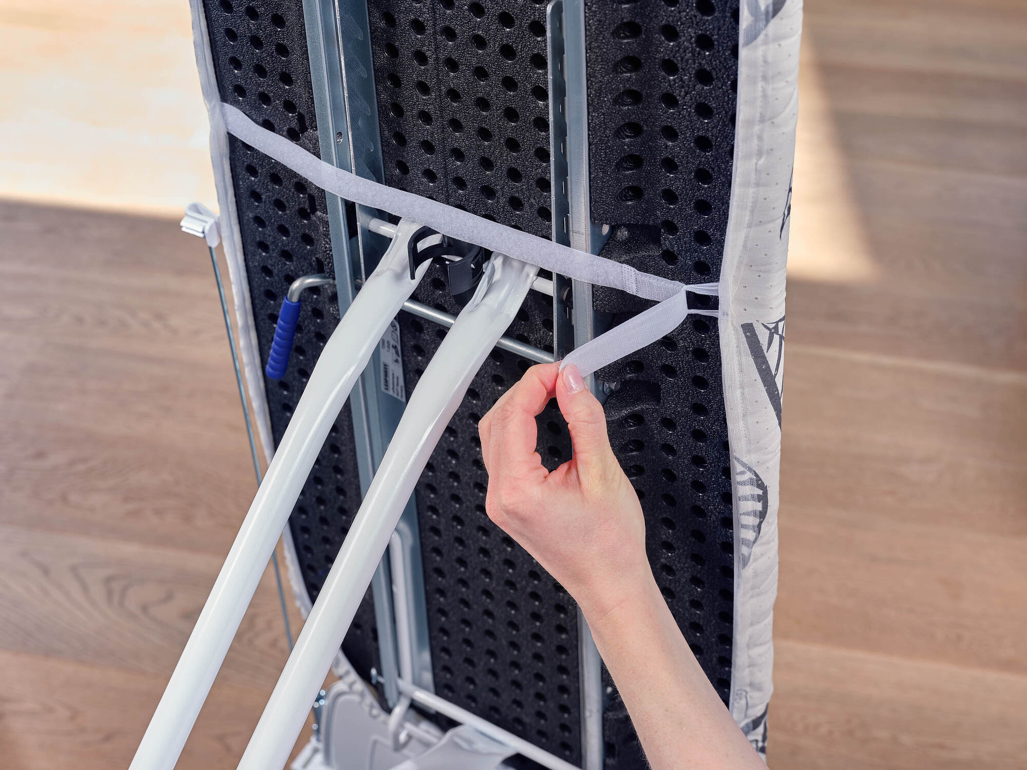 Ręka zapina rzep do ramy deski do prasowania.