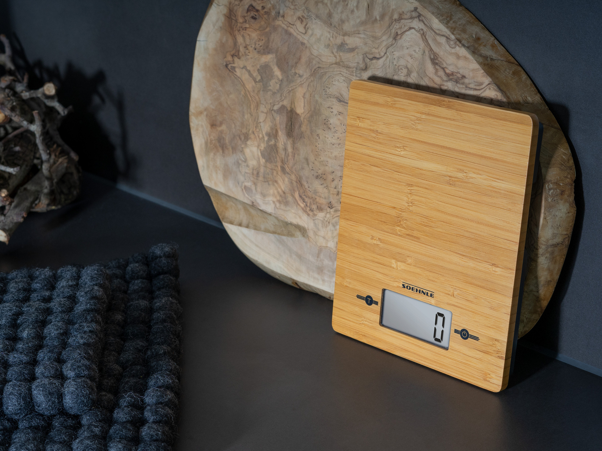 Eine Holzküchenwaage mit digitaler Anzeige steht neben einem großen Holzbrett.