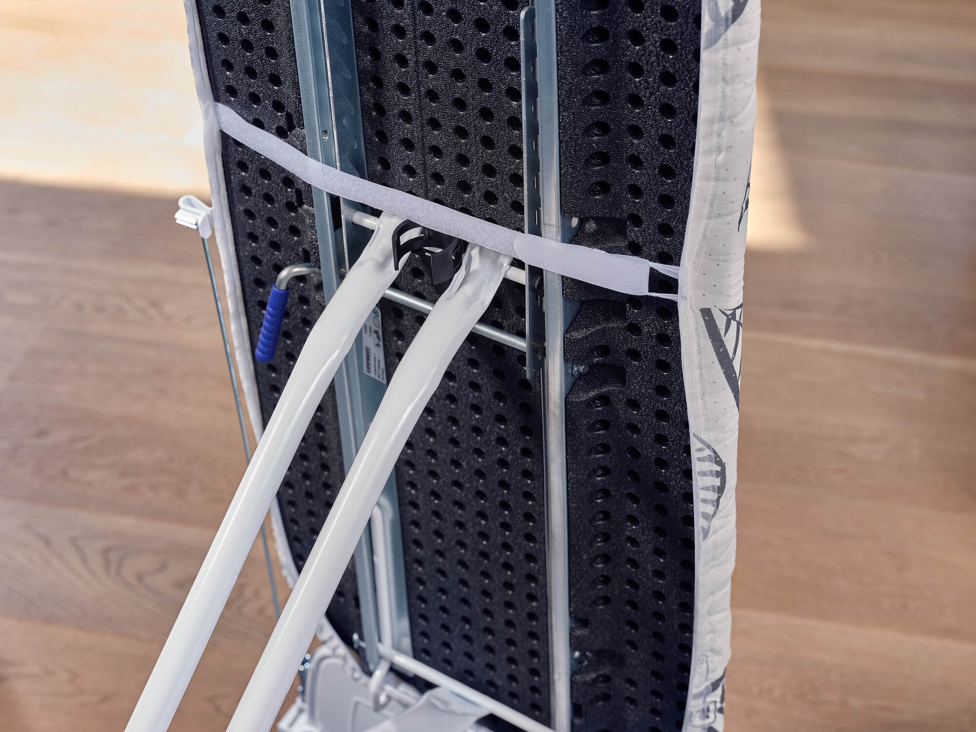 Deska do prasowania z czarną perforowaną deską i białymi rurkami.