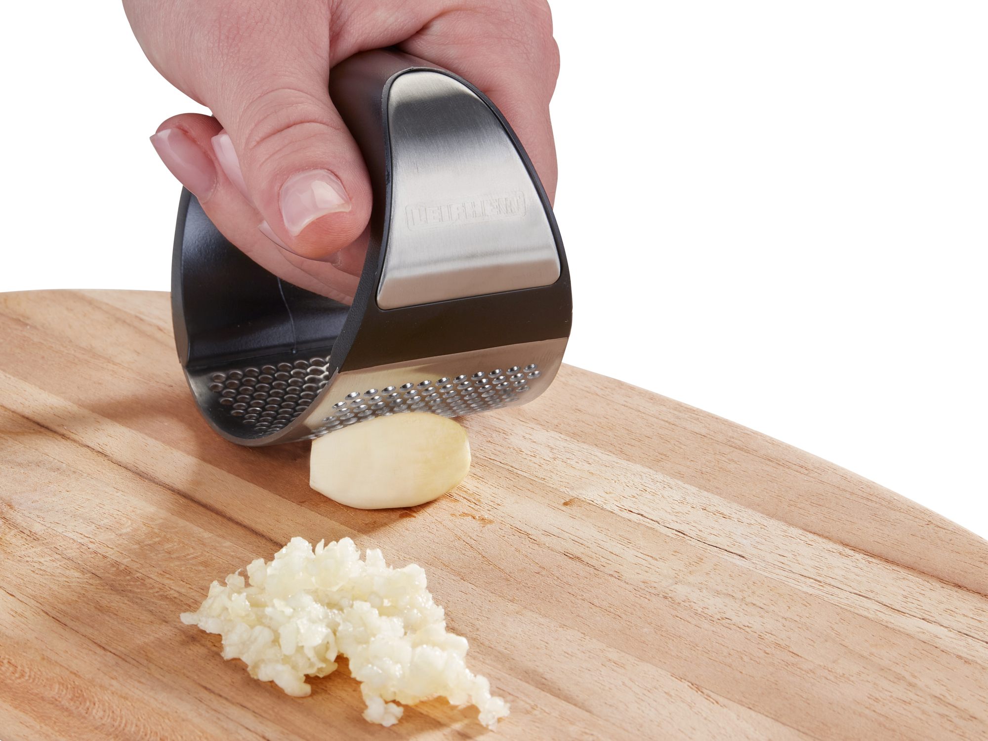 Dłoń dociska czosnkownicę do ząbka czosnku na drewnianej desce.