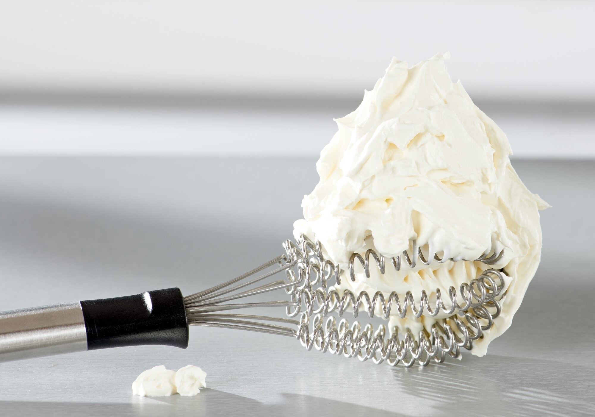 Un batidor con mango negro cubierto de crema blanca.