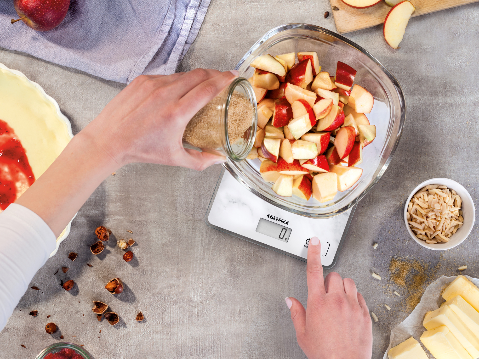 Ręka wsypuje cukier ze słoika do miski z kawałkami jabłek na wadze.
