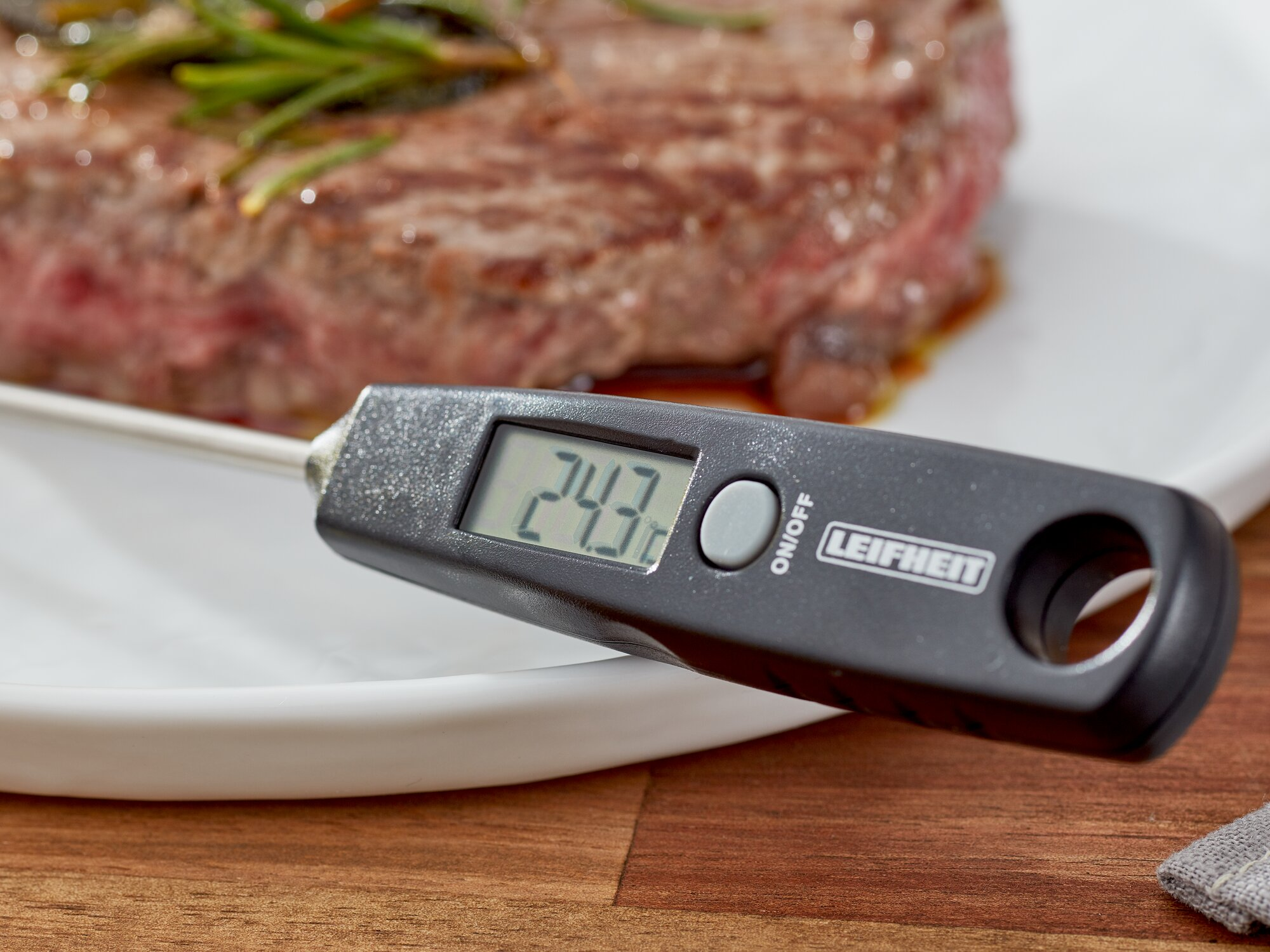 Un termometro digitale per carne mostra 24,3°C accanto a una bistecca su un piatto.