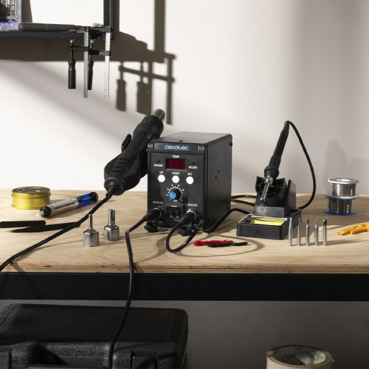 Utensili per riparazioni elettroniche su tavolo in legno con stazione saldante, pistola aria calda e accessori.