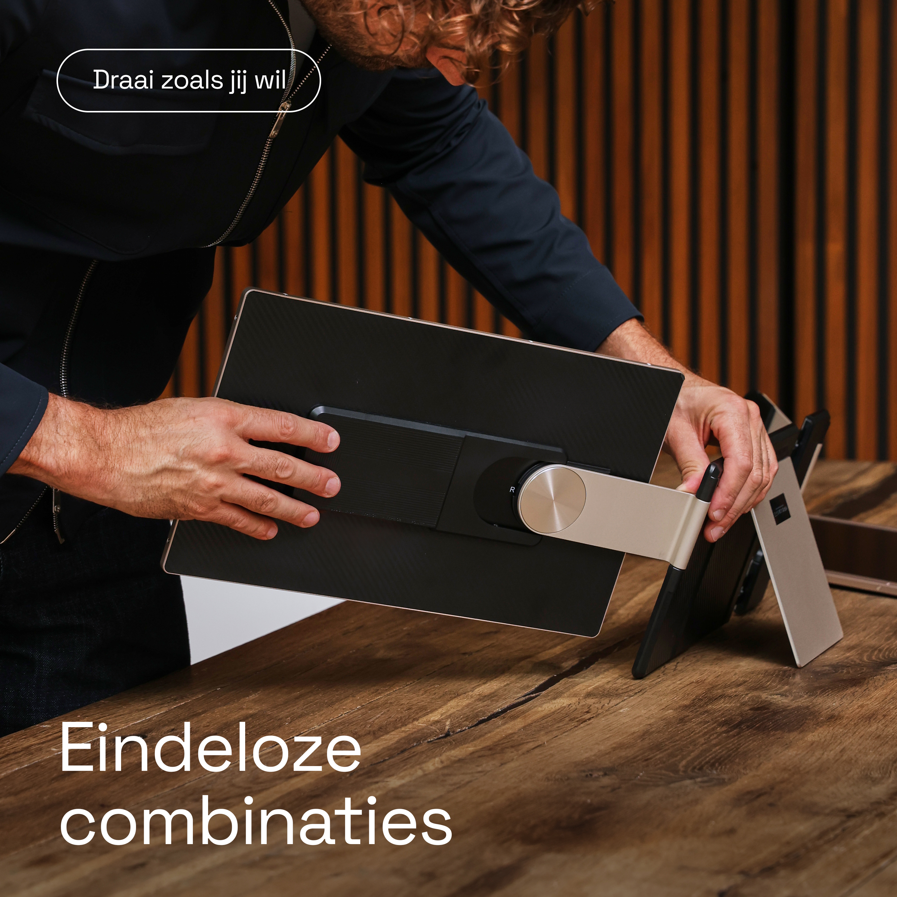Homme installe écran noir sur table en bois. Arrière avec pied visible.