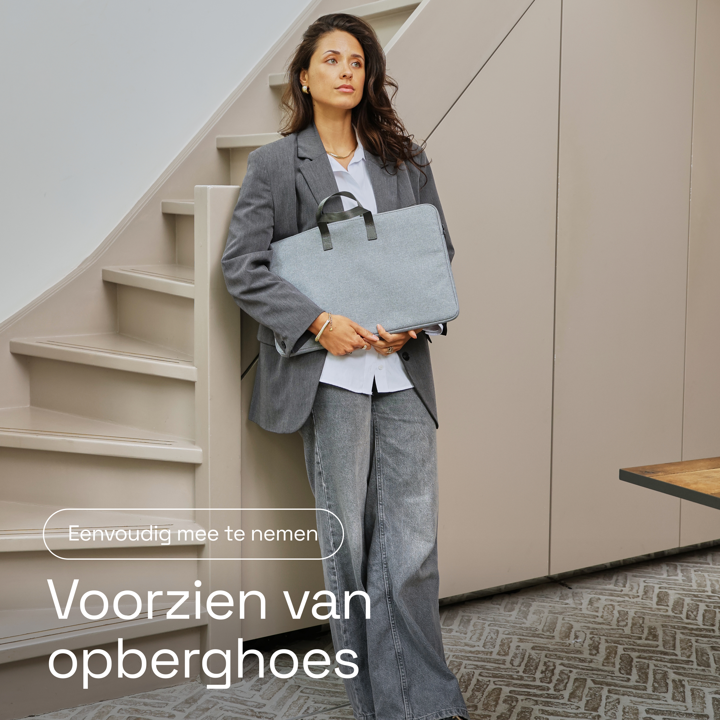 Een vrouw in een grijs pak houdt een grijze laptoptas vast.