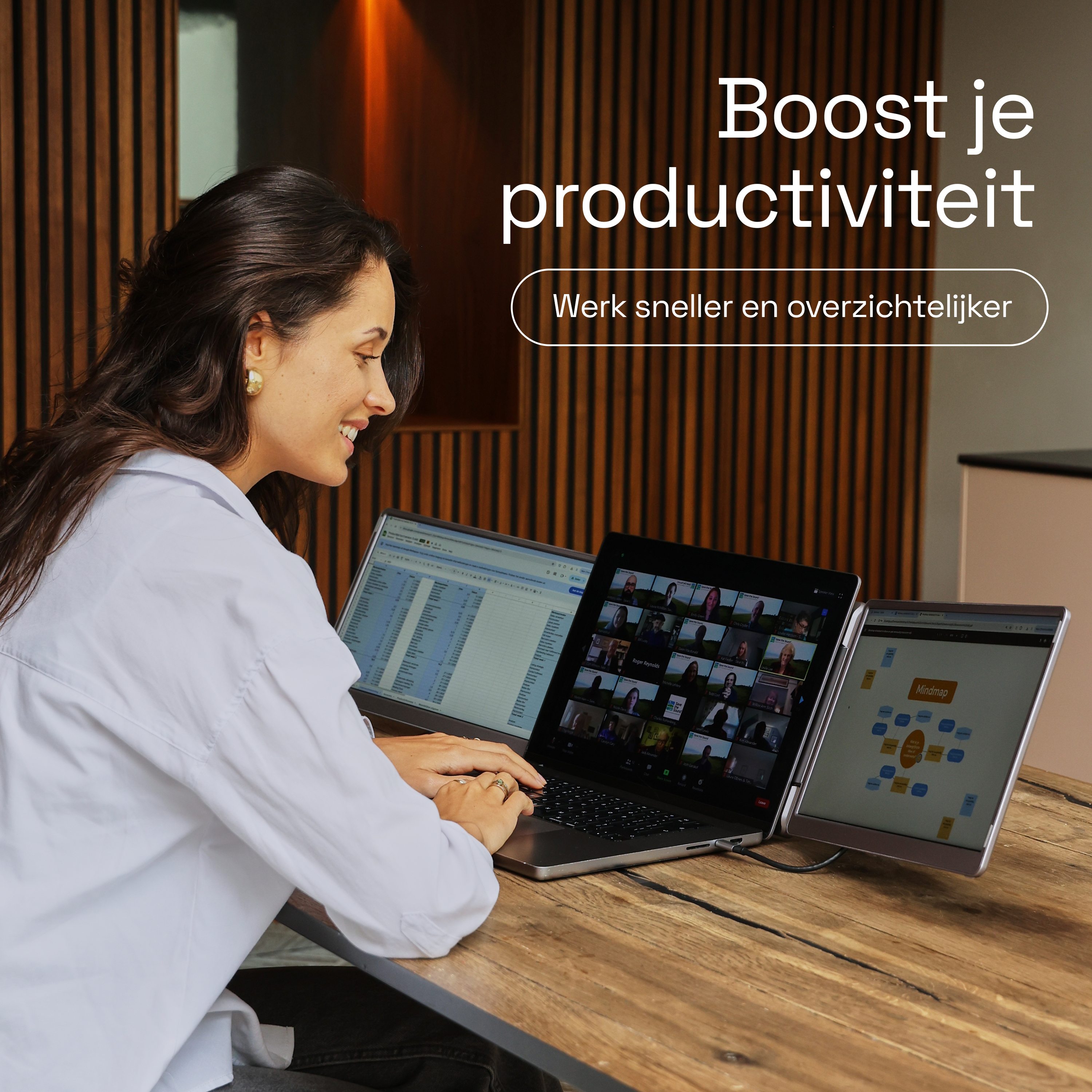 A woman works on three screens. The middle screen shows a video meeting.