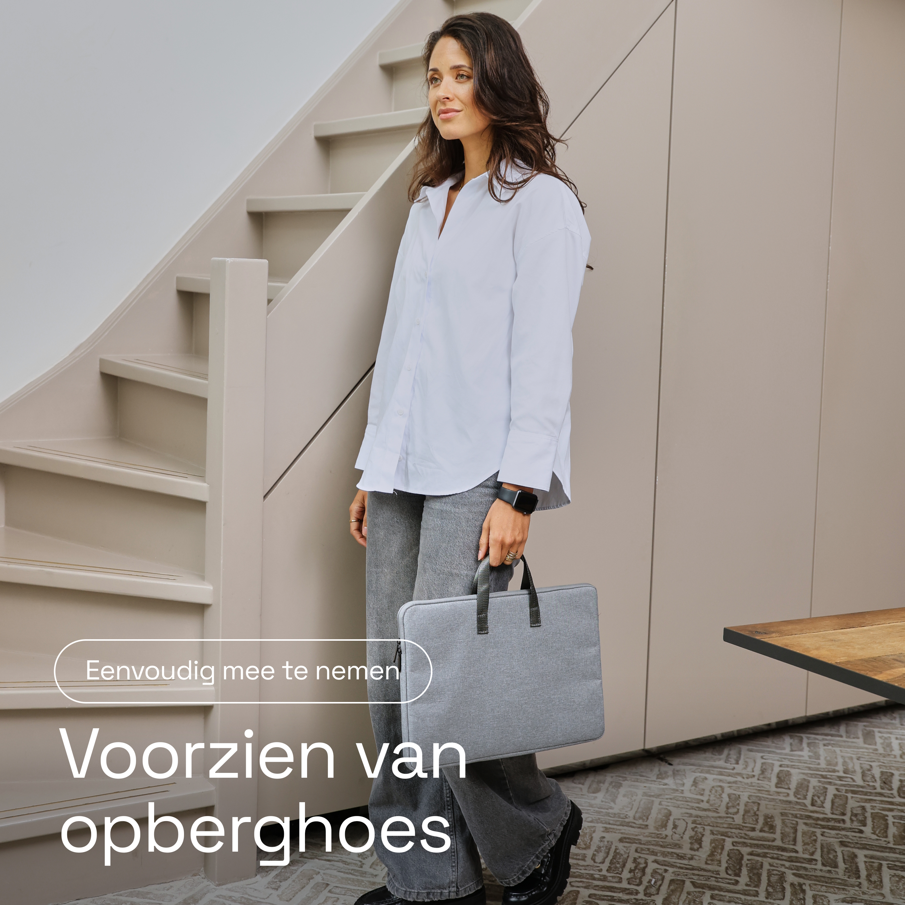 A woman in a white shirt and gray pants carries a gray laptop bag.