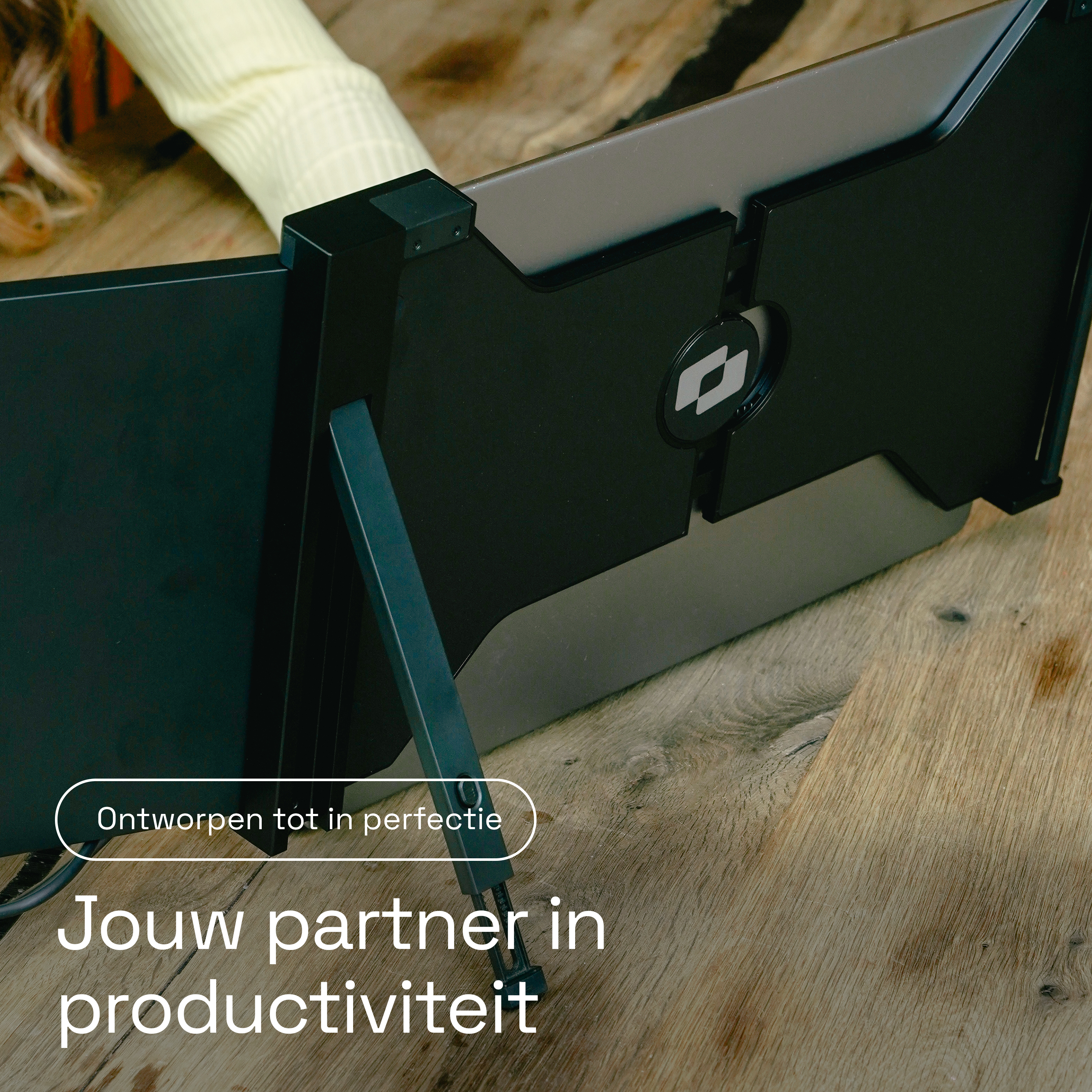 Een draagbare monitor staat op een houten vloer naast een persoon in een lichtgekleurde trui.