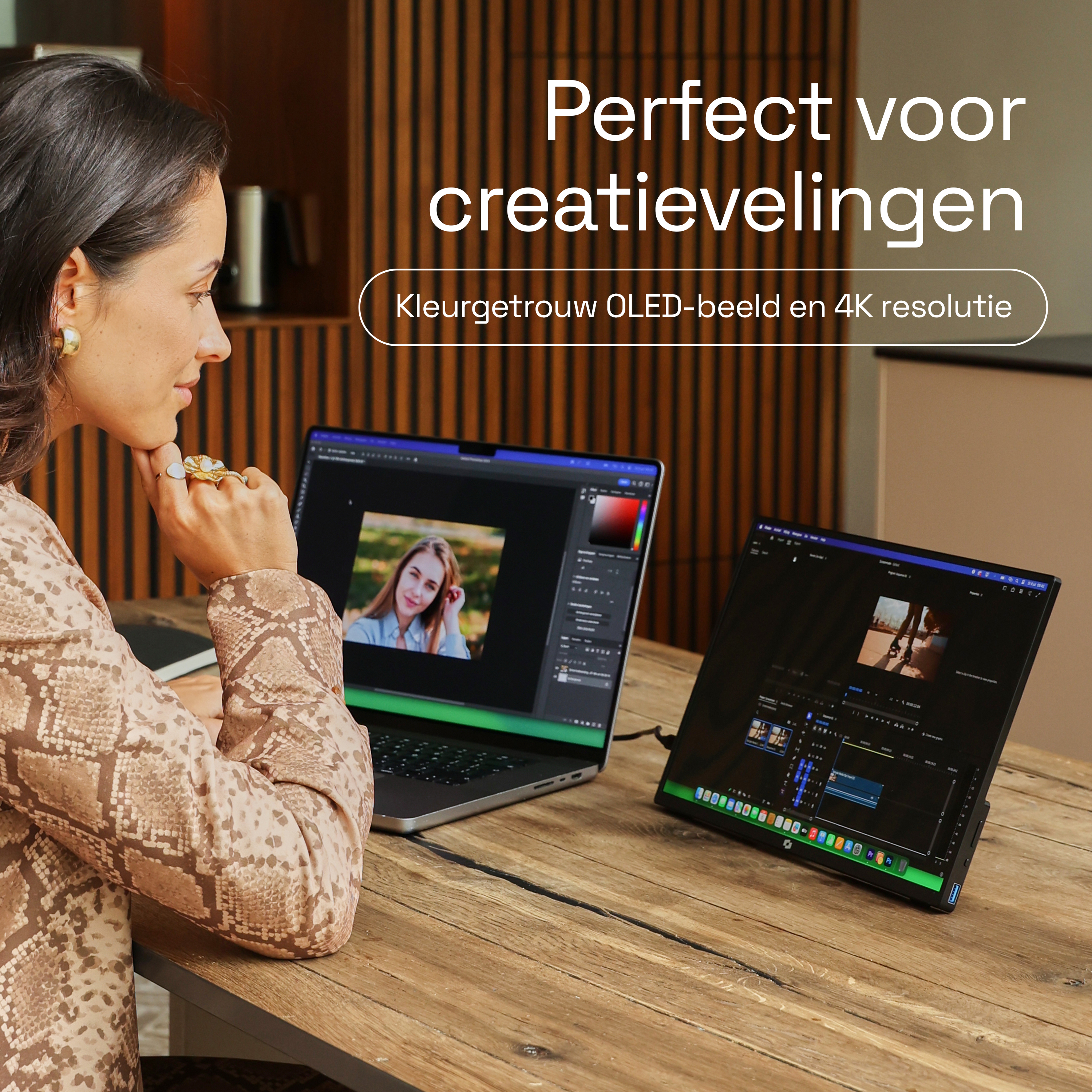 Een vrouw zit aan een houten tafel en gebruikt een laptop en een externe monitor.
