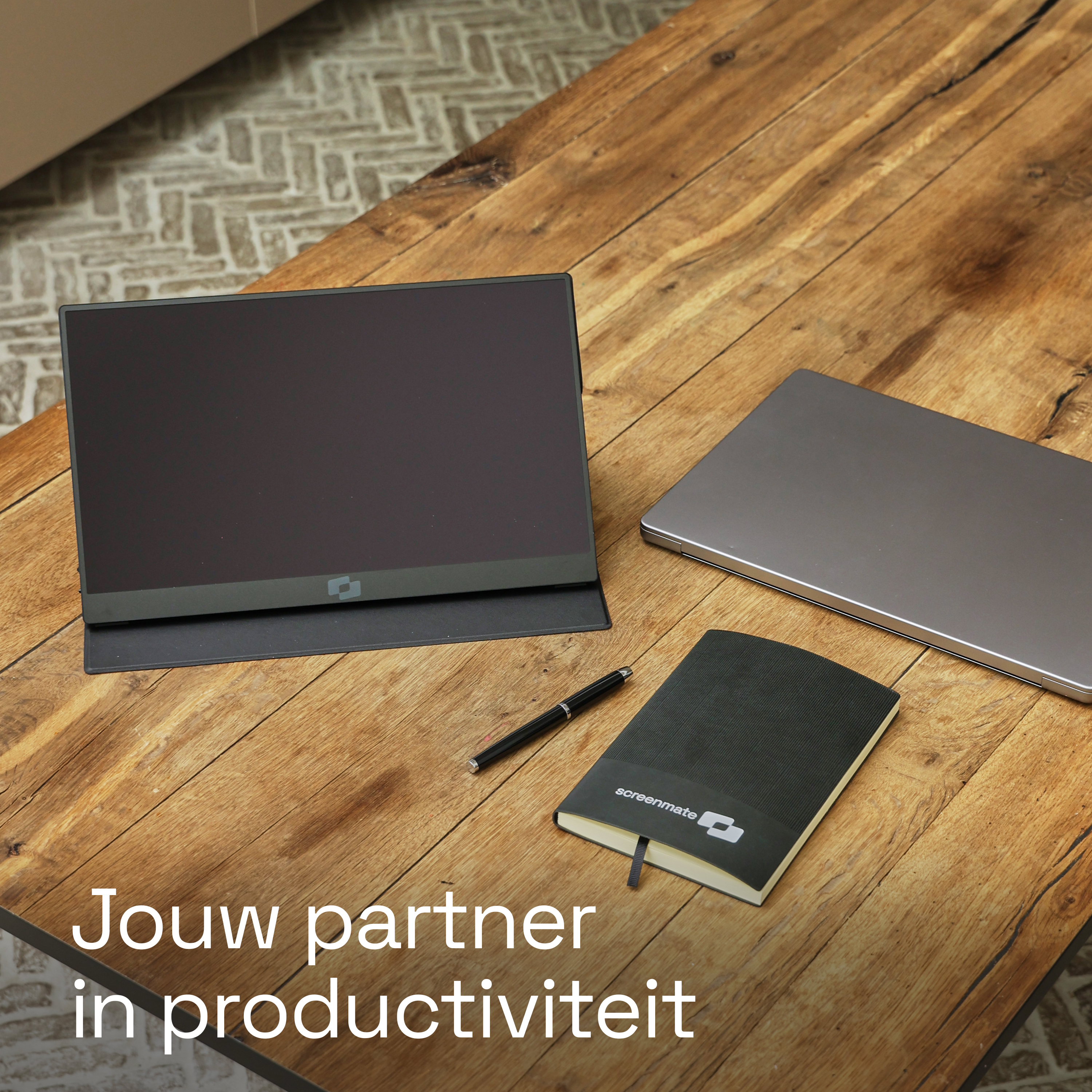 Een draagbare monitor, laptop, notitieboekje en pen op een houten tafel.