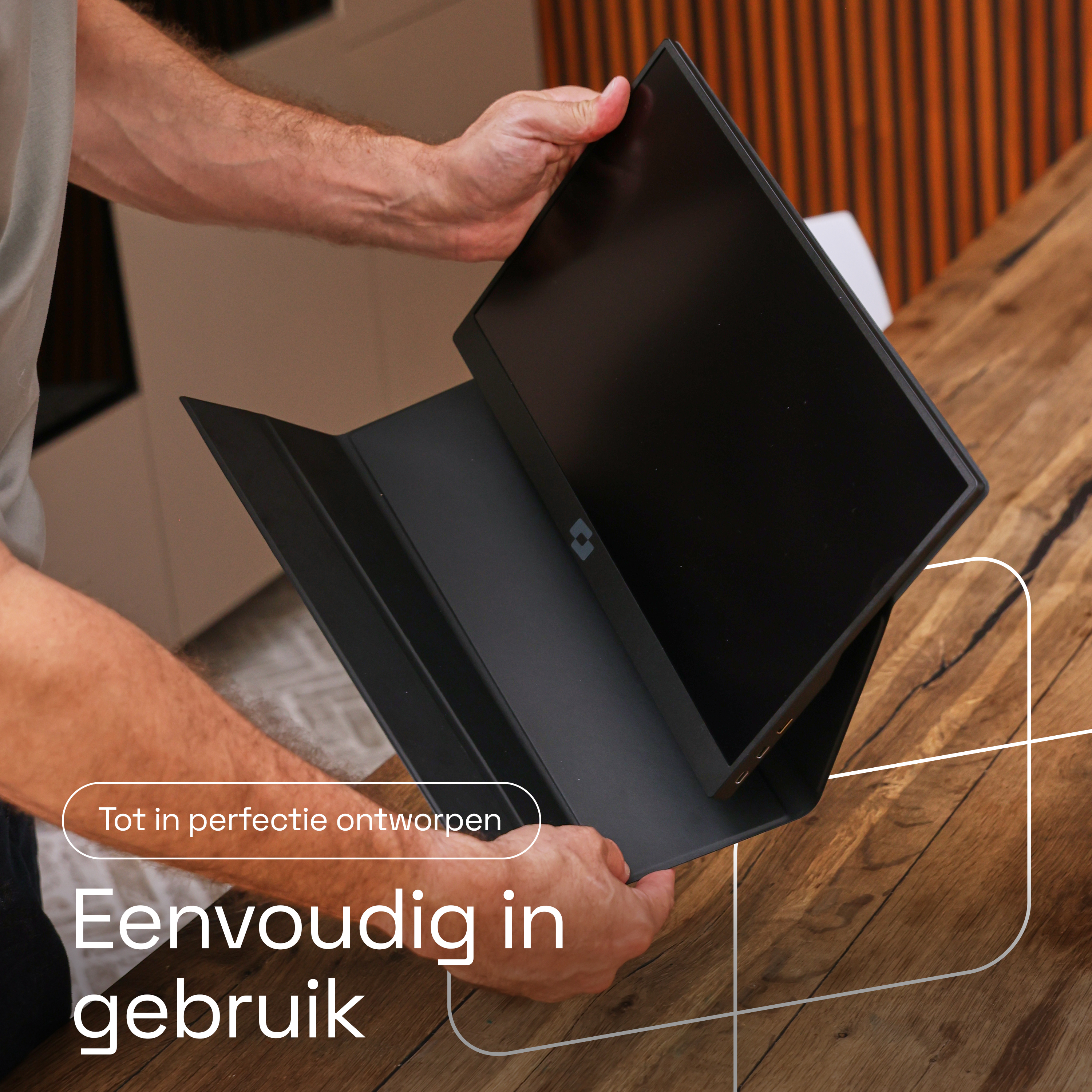 Een man houdt een zwarte monitor met beschermhoes op een houten tafel.