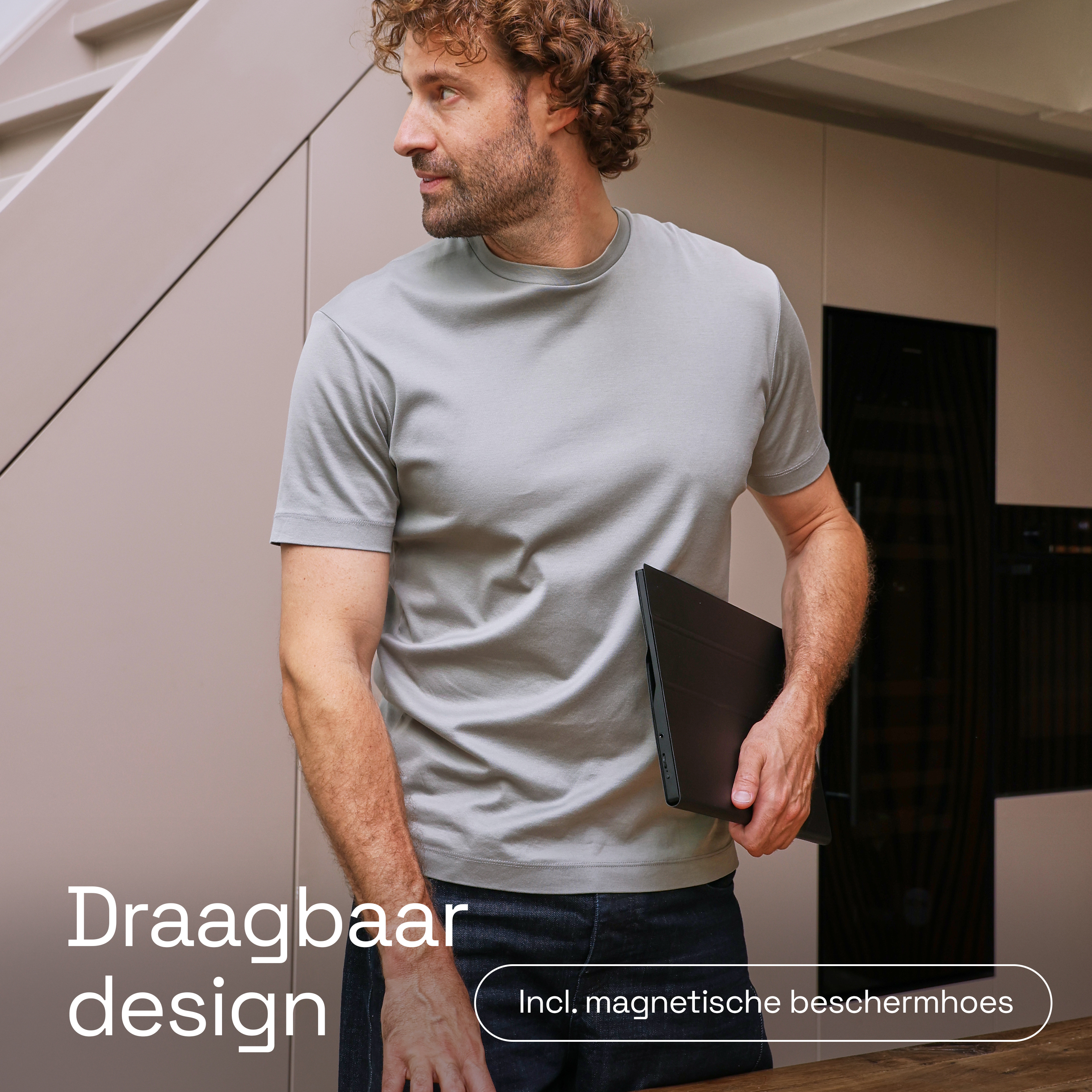 Man met krullend haar houdt een zwarte tablet vast in een moderne kamer.