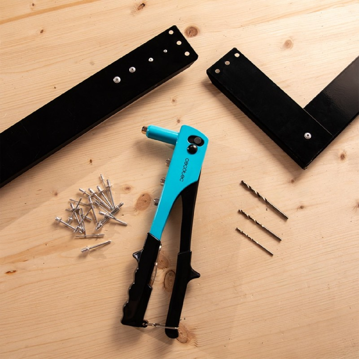 Una rivettatrice blu con rivetti, punte da trapano e parti metalliche nere su legno.