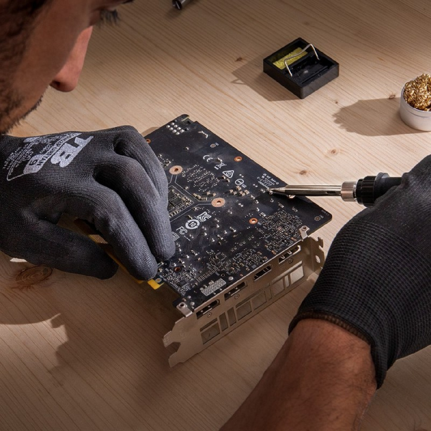 Uomo con guanti salda un circuito stampato su un tavolo di legno.