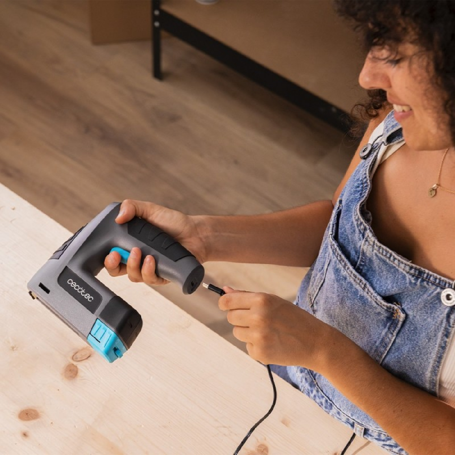 Una donna in salopette collega un utensile elettrico grigio e blu a un cavo.