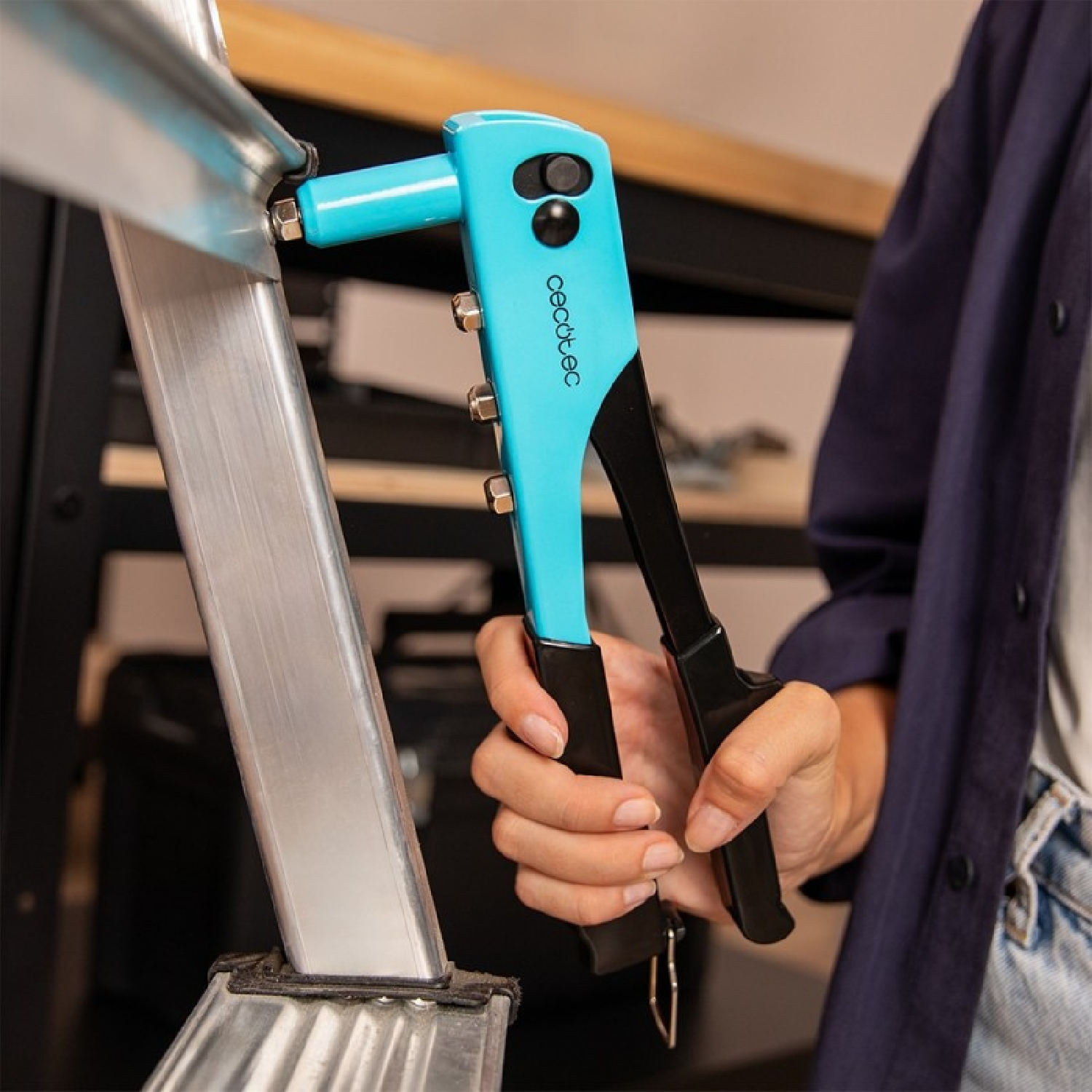 Una mano usa una pistola per rivetti blu per fissare parti metalliche.