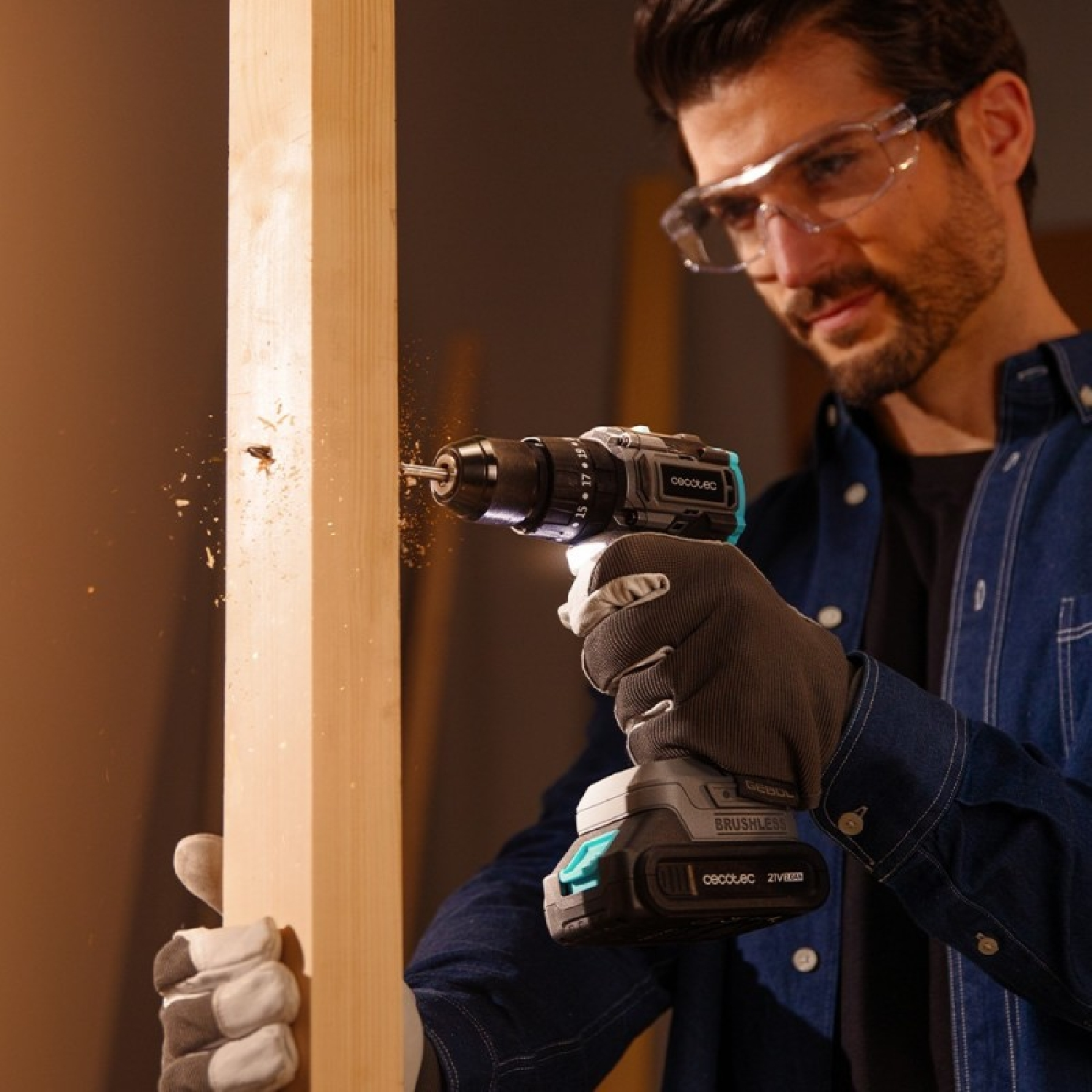 Hombre taladrando madera con taladro inalámbrico, con gafas y guantes.