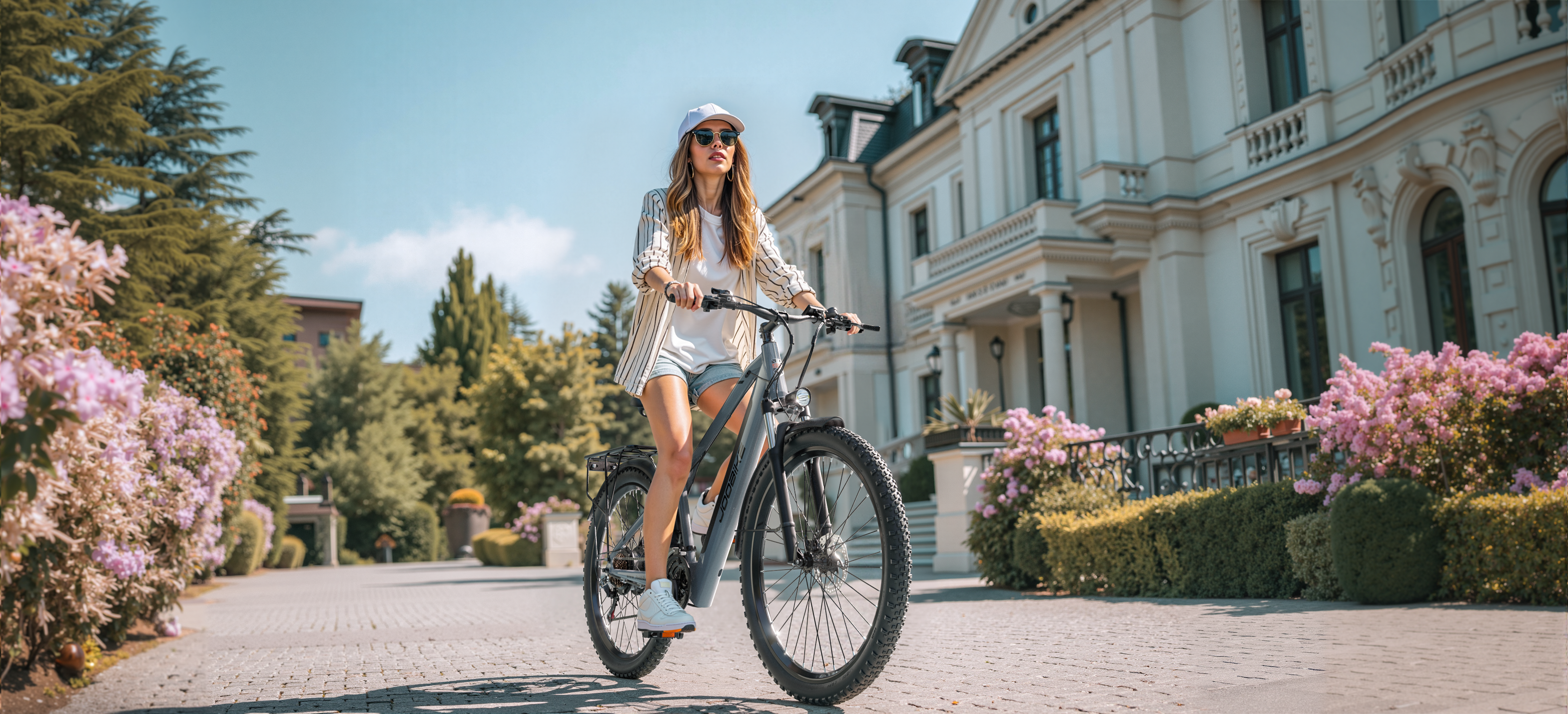 Frau fährt E-Bike vor luxuriösem Gebäude mit Bäumen und Blumen.