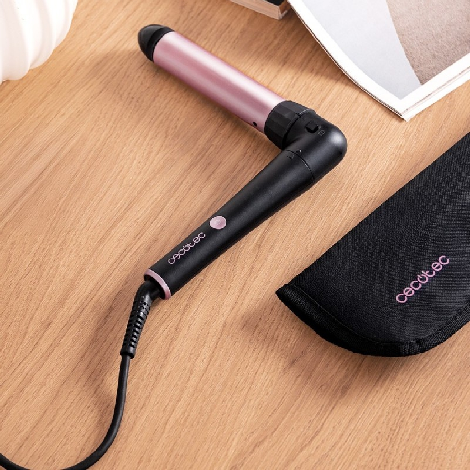 Un arricciacapelli rosa e nero con cavo poggia su una superficie di legno accanto a una custodia nera.